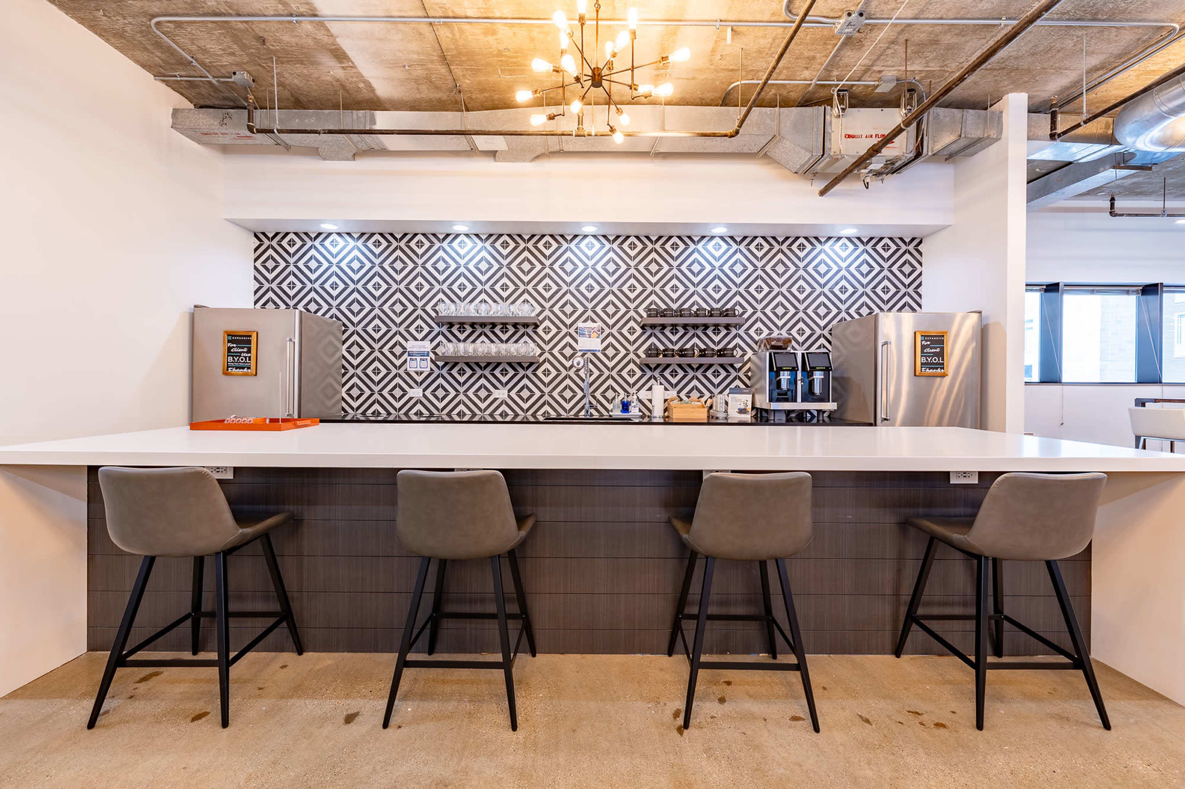 The image shows a modern kitchen bar area with a sleek countertop, four high stools, and a patterned tile backsplash.