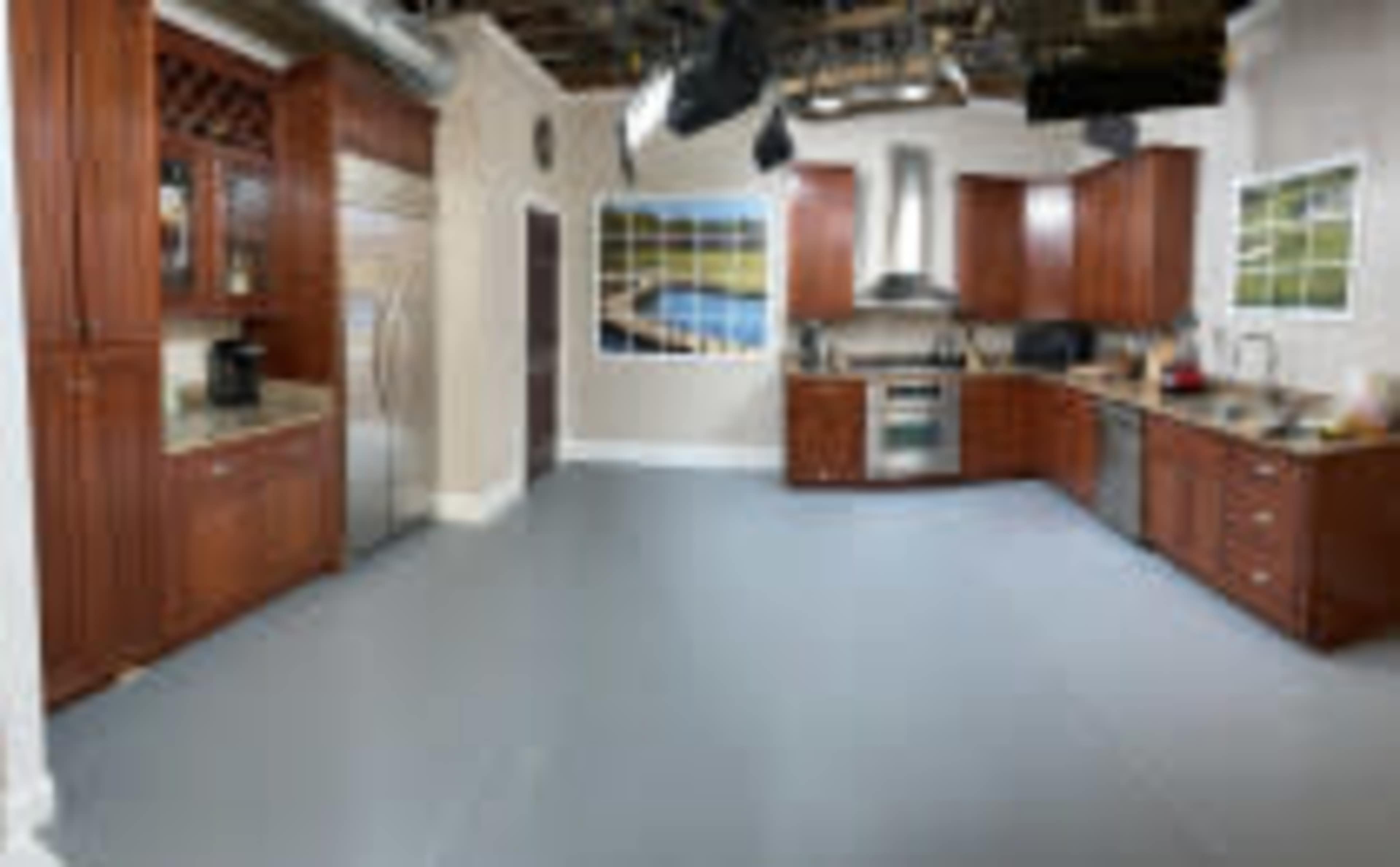 A modern kitchen with wooden cabinetry, stainless steel appliances, and a light gray floor.