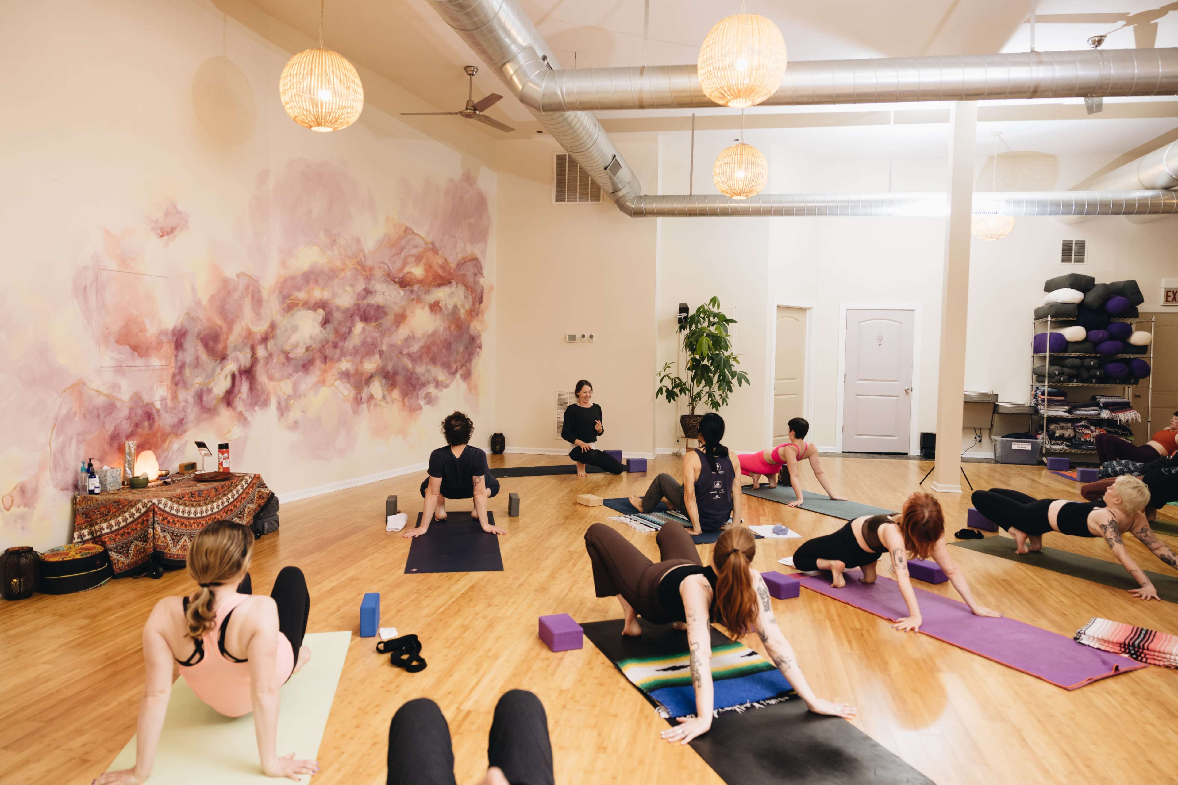 A yoga class is taking place in a studio with participants practicing various postures on mats while a teacher provides guidance at the front.