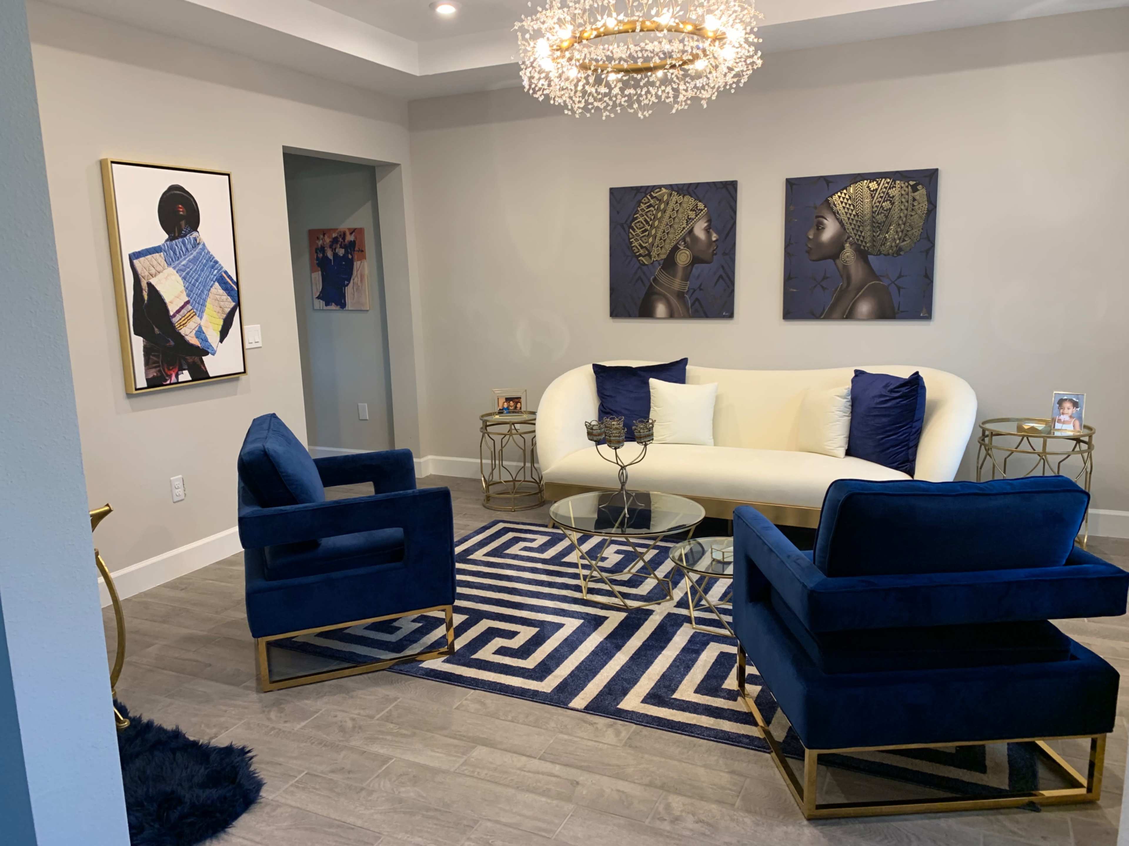 A modern living room with a white sofa, two blue chairs, a glass coffee table, and artwork on the walls.