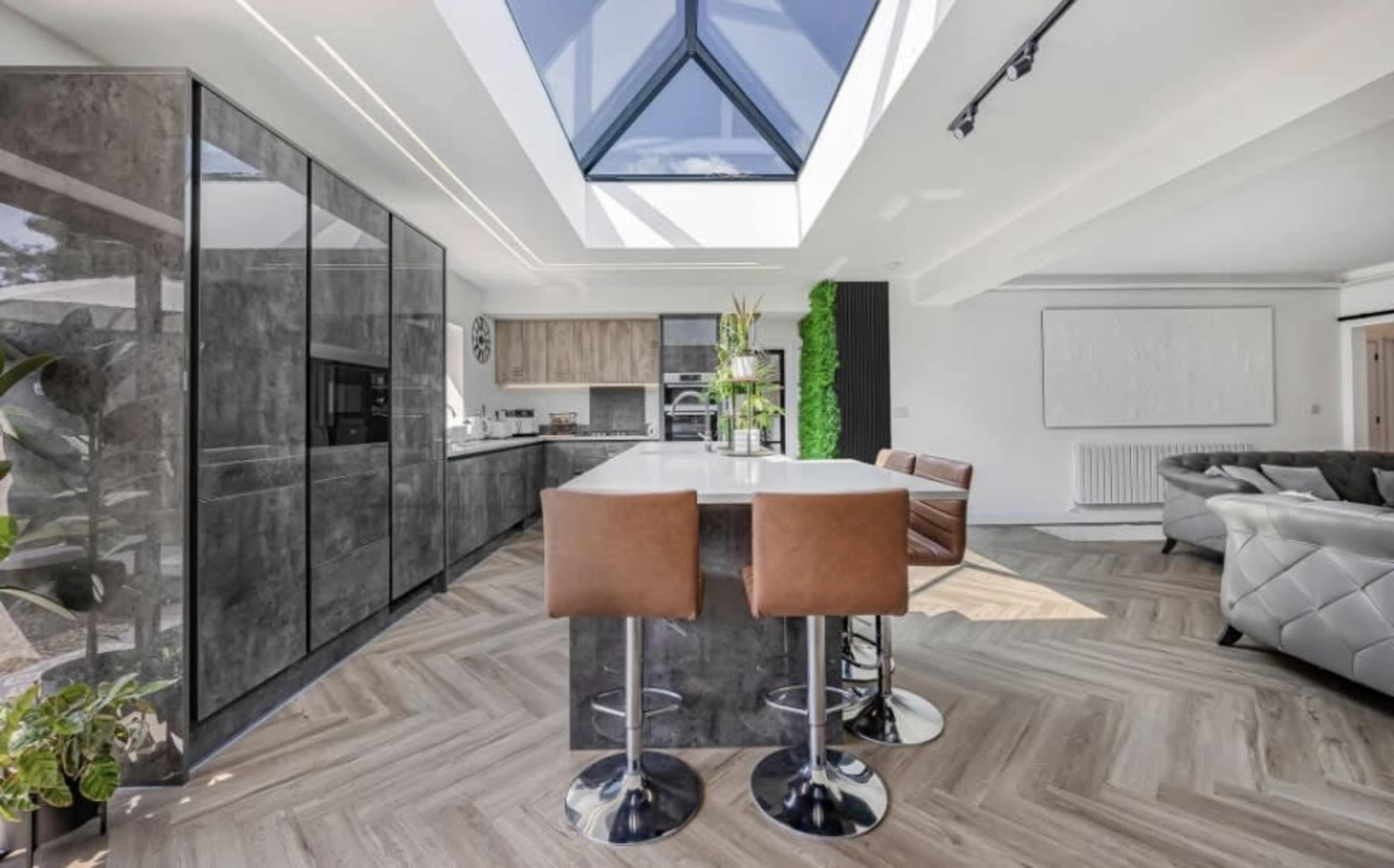 The image shows a modern kitchen featuring dark cabinets, a central island with bar stools, and a skylight that illuminates the space.