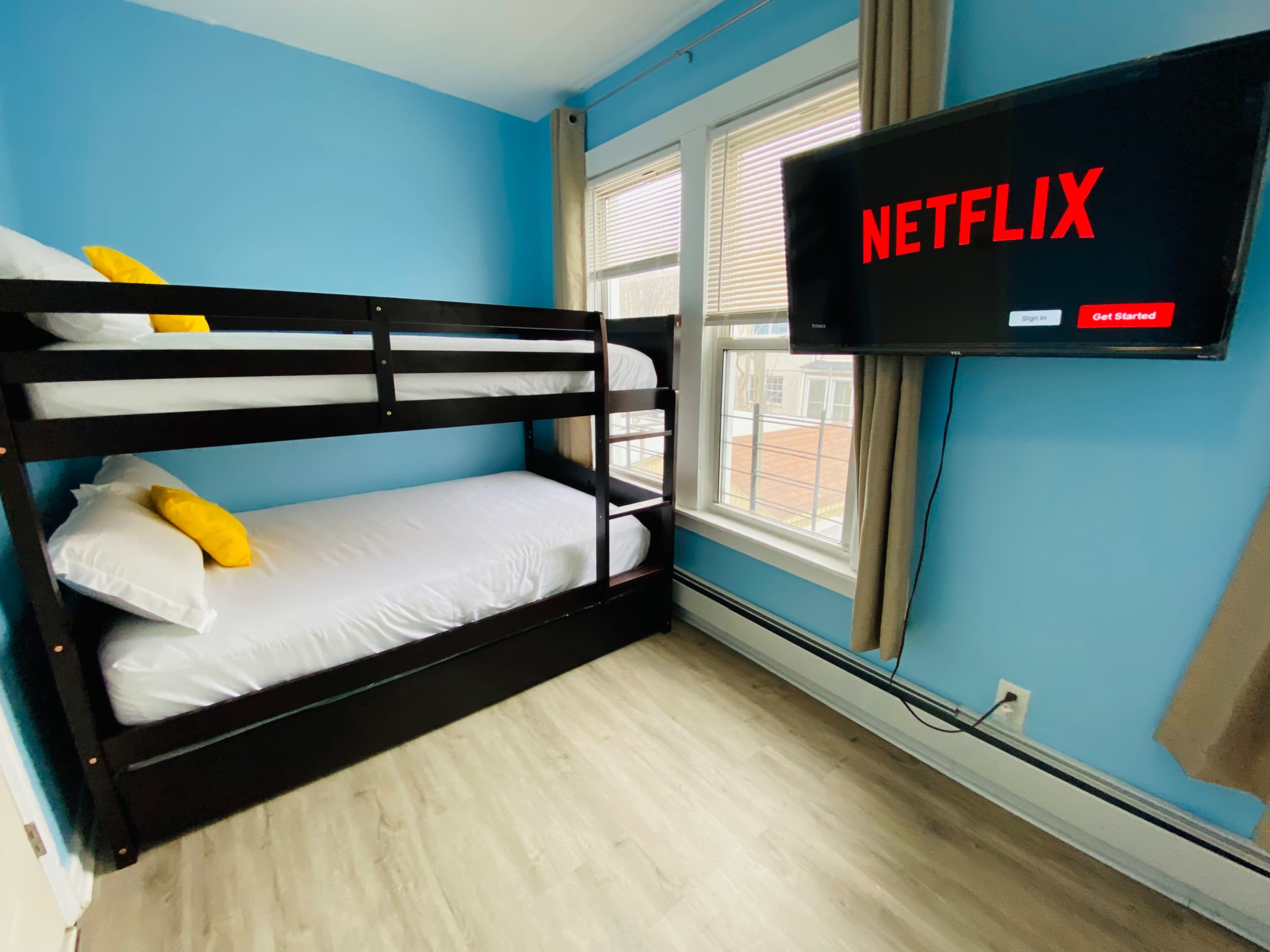 The image shows a bedroom with a bunk bed against a blue wall and a television displaying the Netflix logo.