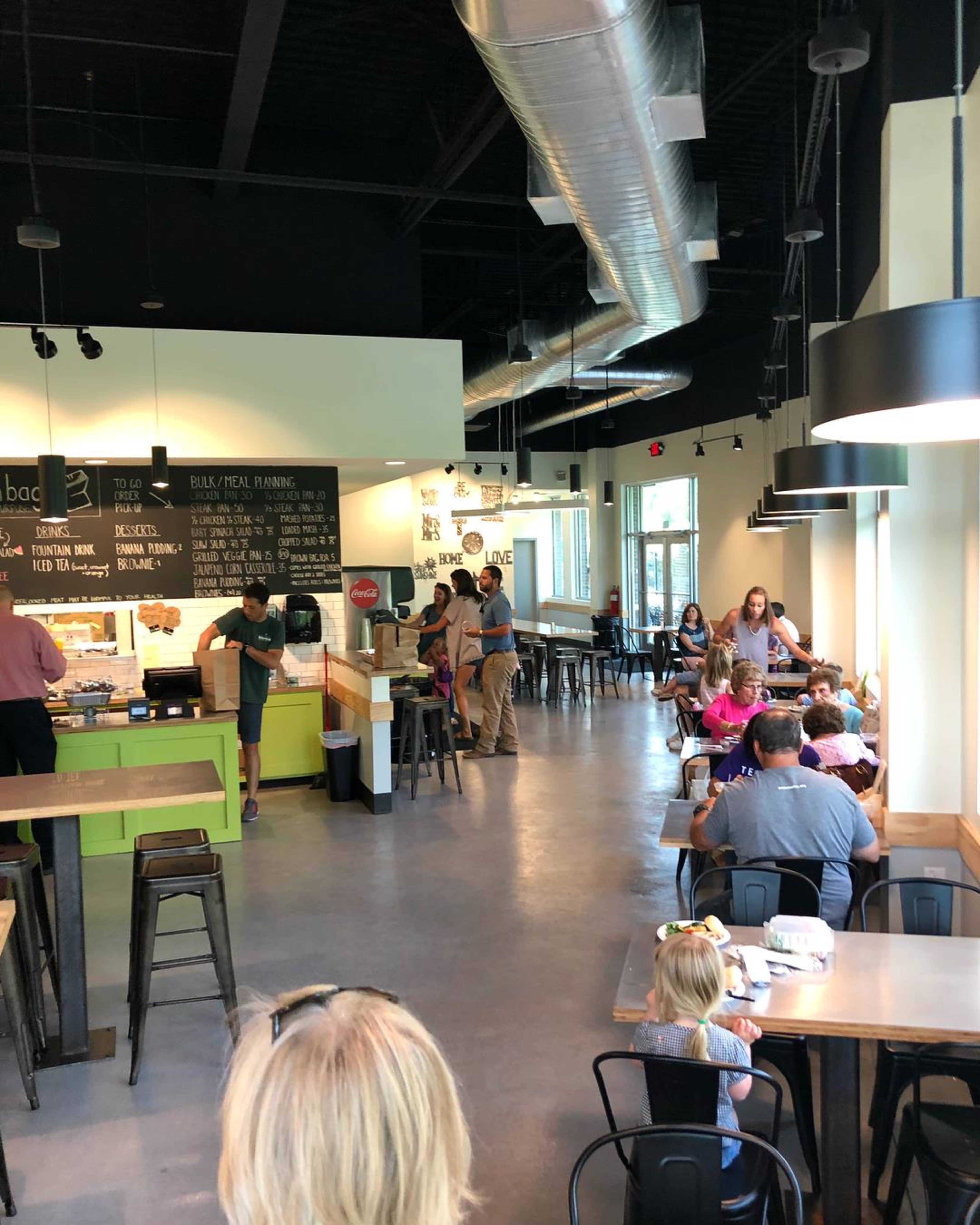 A modern café interior with a variety of seating arrangements, including some patrons at tables and others in line at a service counter.