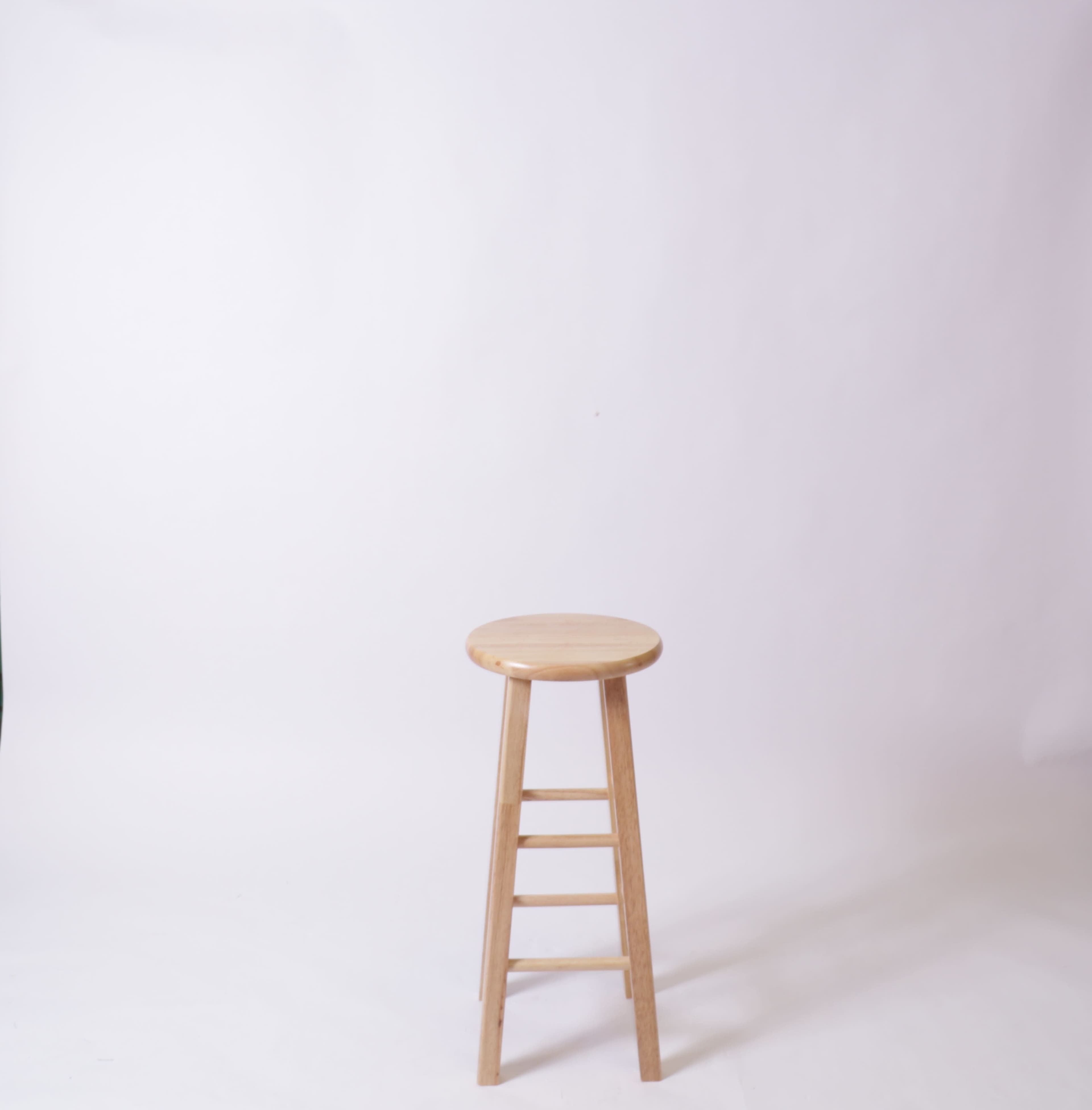 A wooden stool with a round seat and four legs stands against a plain white background.