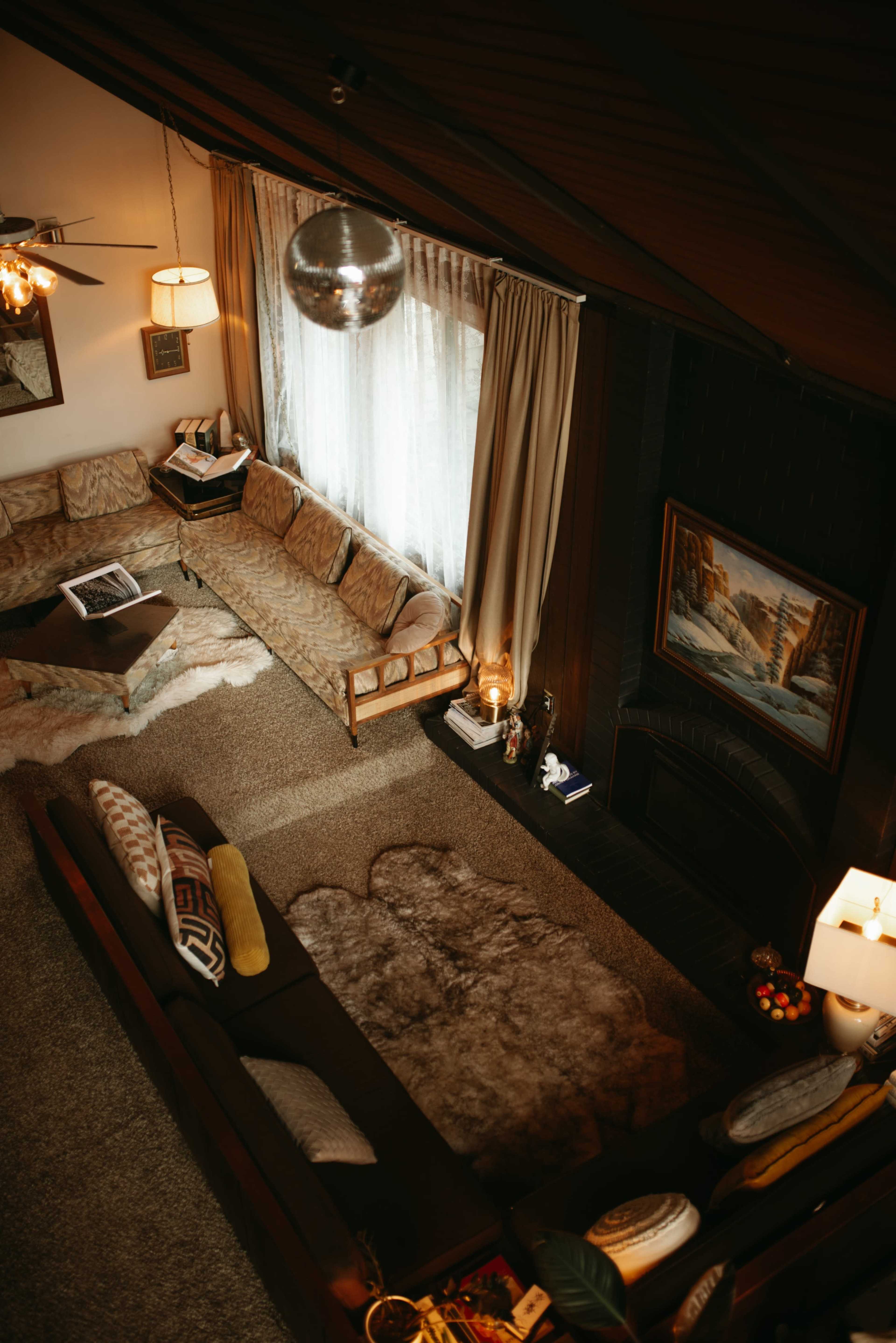 The image shows a cozy living room with two couches, a round coffee table, a large rug, and a window draped with curtains, all arranged around a fireplace.