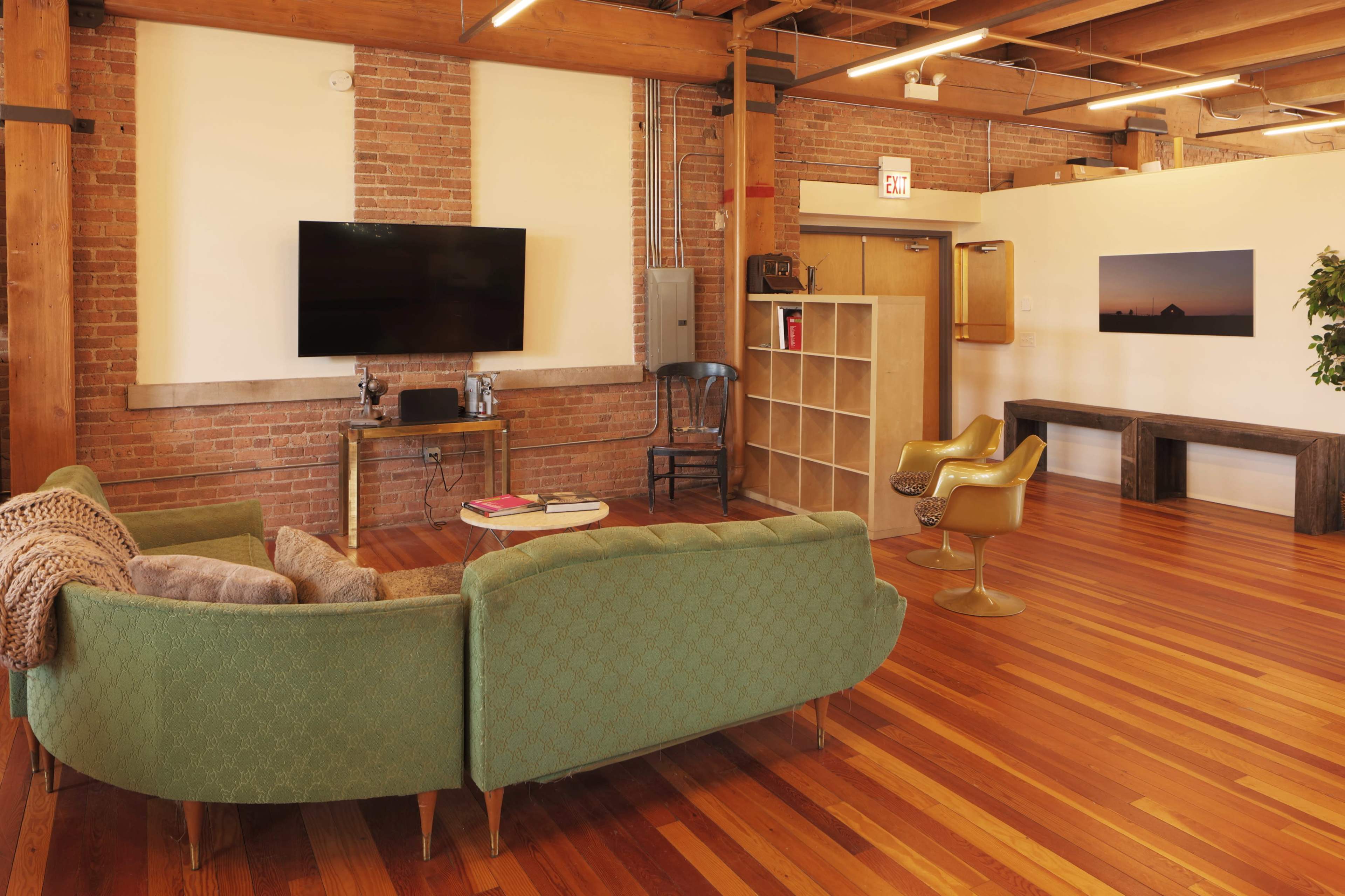A modern living space with a green couch, a television mounted on a brick wall, and wooden flooring.