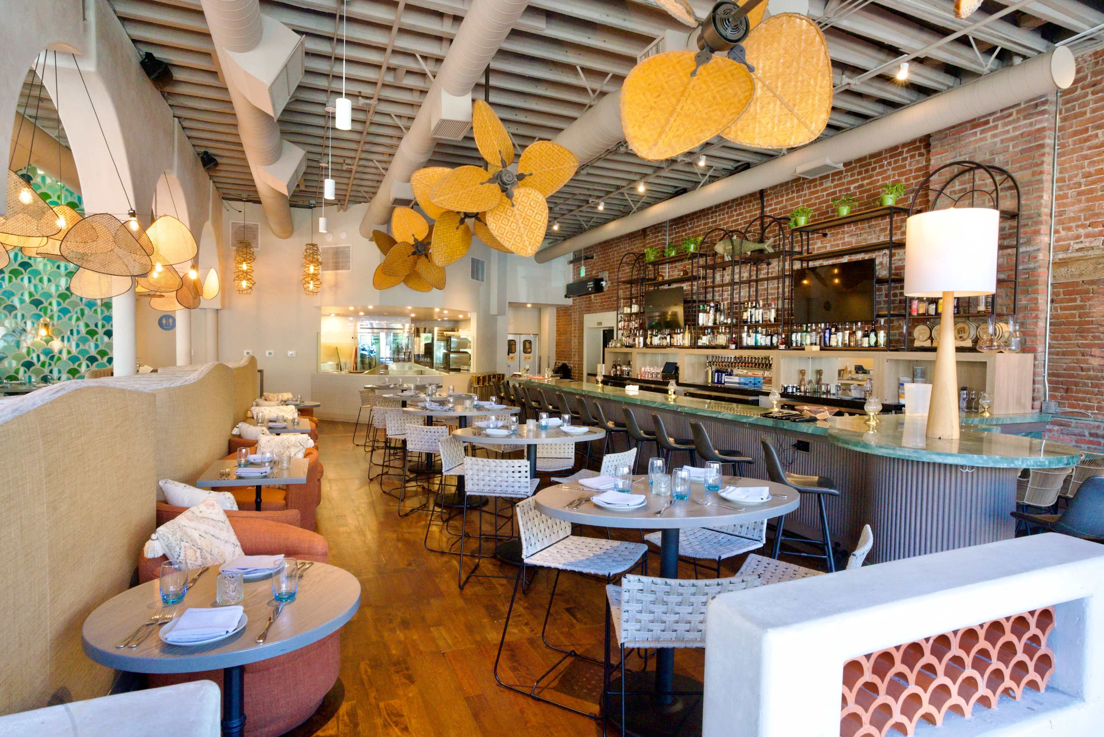 The image shows a stylish restaurant interior featuring wooden floors, modern seating, and decorative pendant lights hanging from the ceiling.