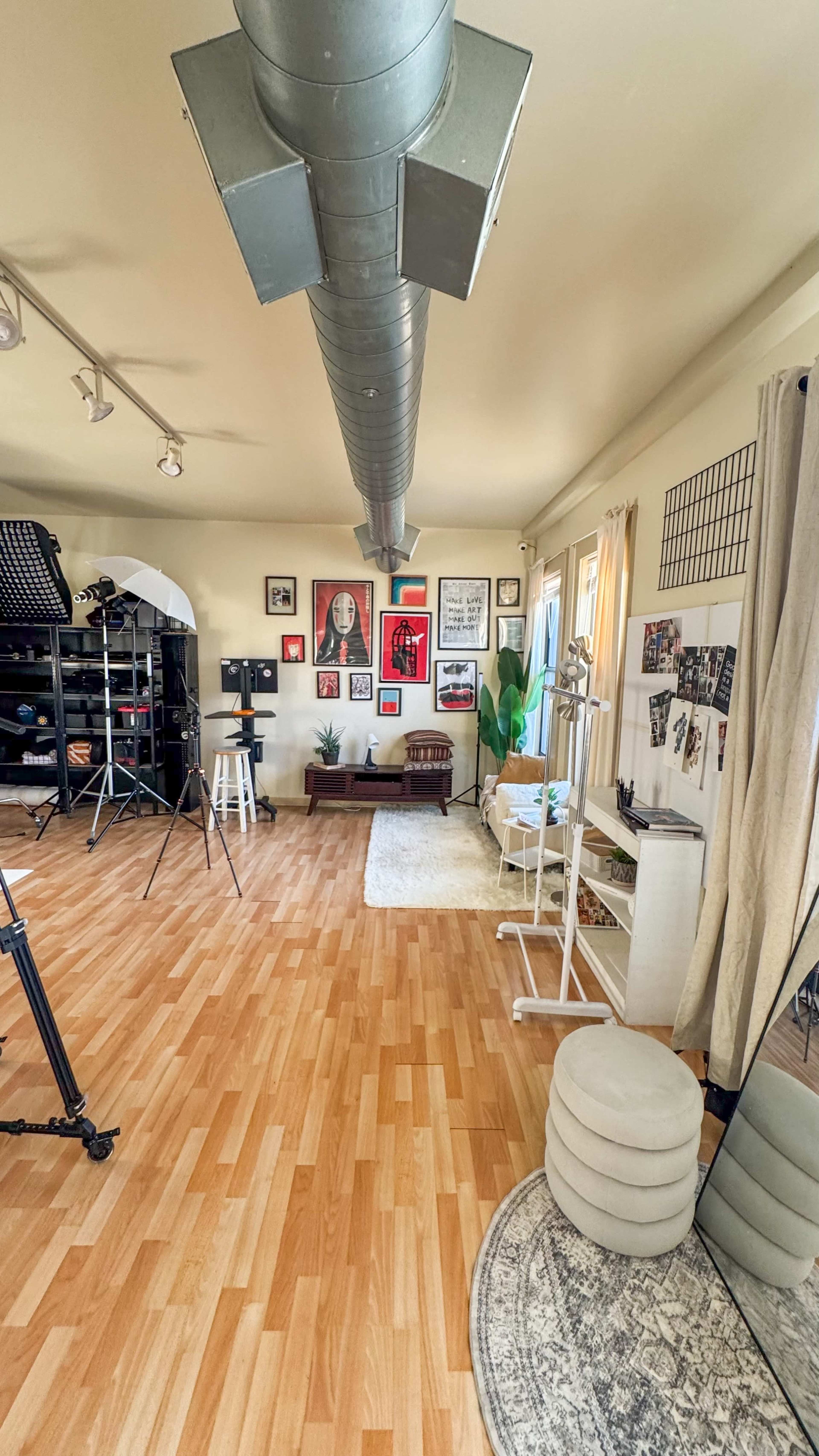 The image shows a spacious studio with hardwood floors, equipped with various photo and video equipment, wall-mounted art, and a small seating area.