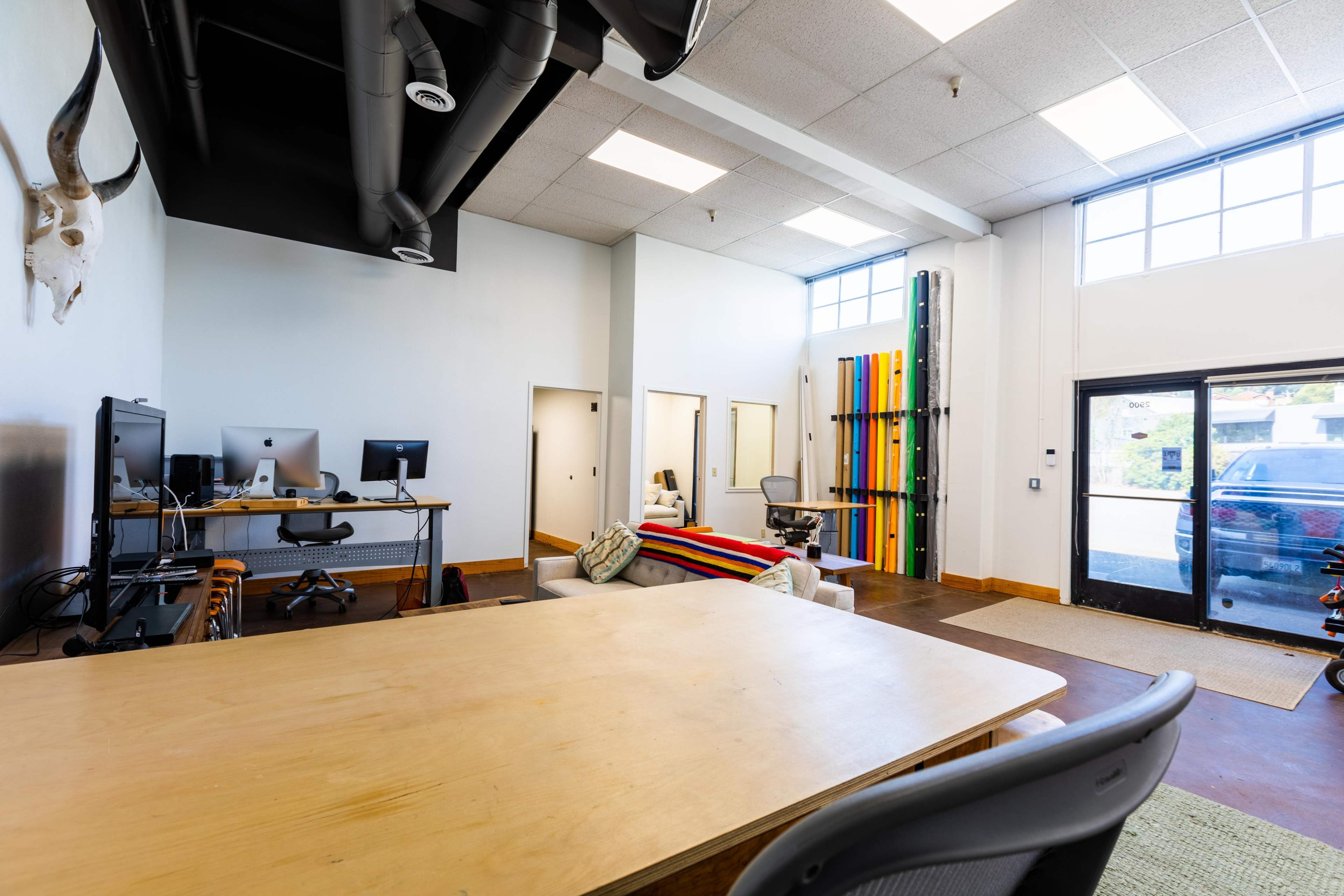 A modern office space with a large wooden table, multiple computers, and colorful vertical panels in the background.