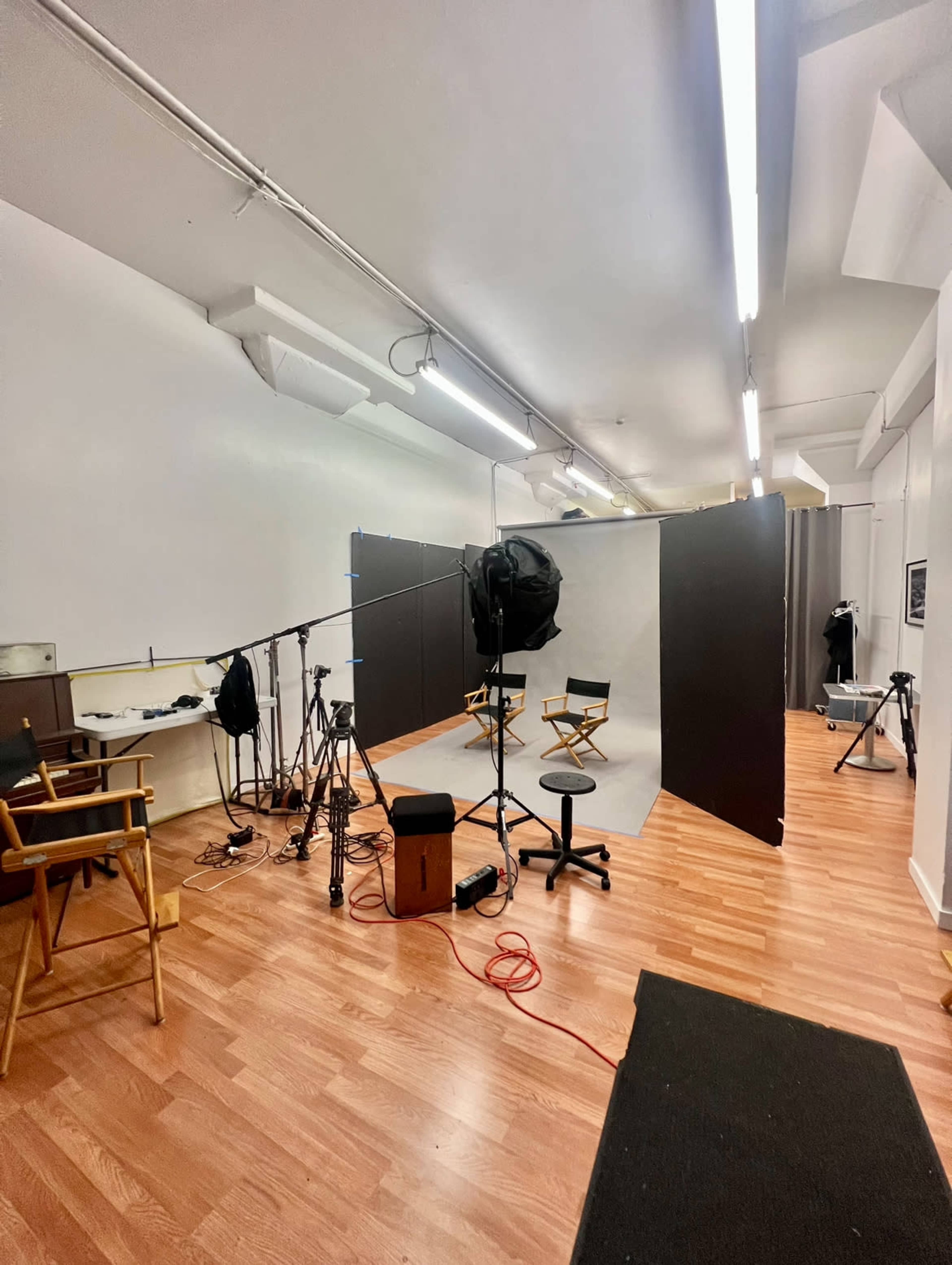 The image shows a photography studio with lighting equipment, a backdrop, and director's chairs arranged for a shoot.