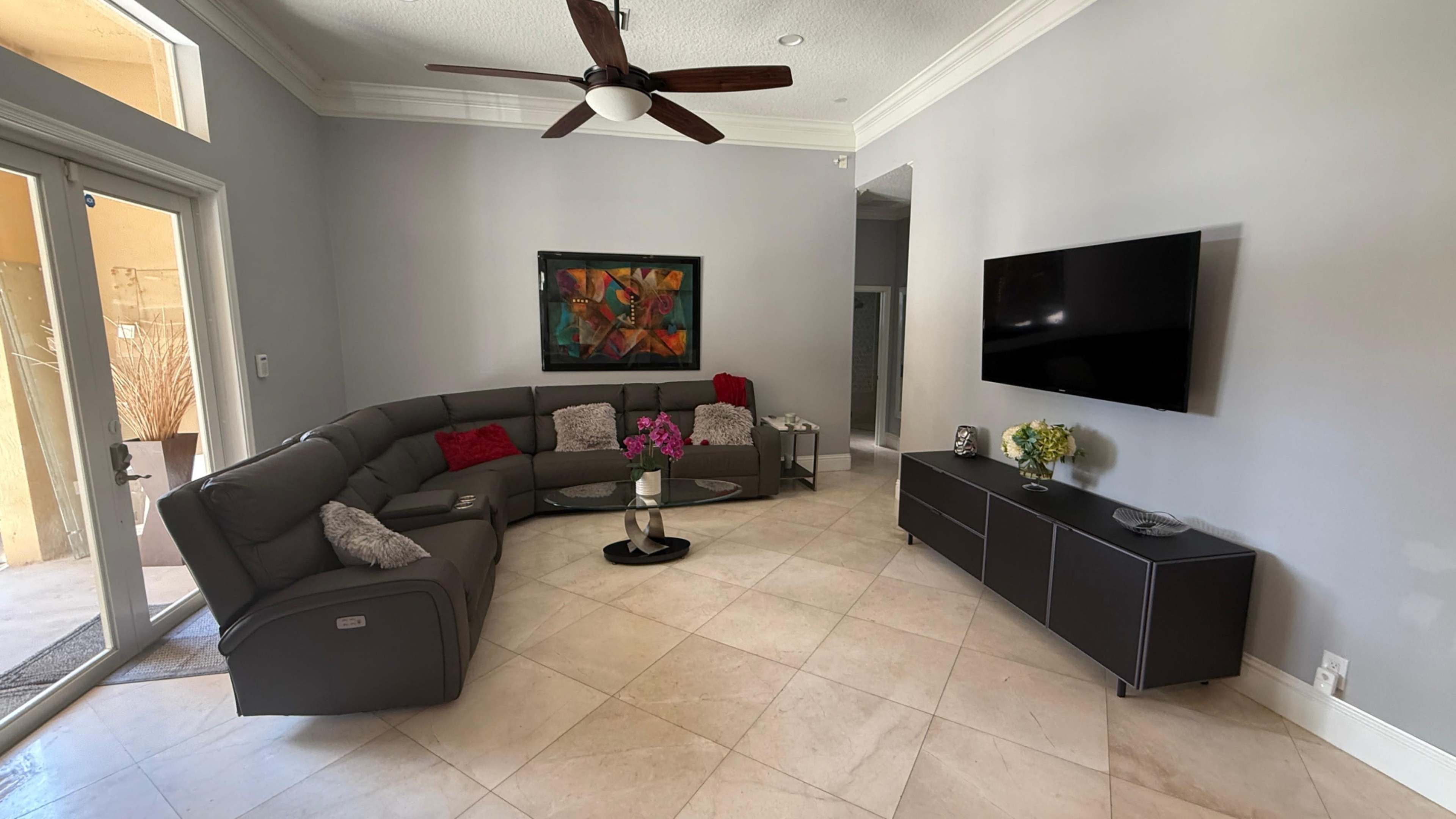 The image shows a modern living room with a sectional sofa, a circular coffee table, a wall-mounted television, and decorative artwork on the wall.