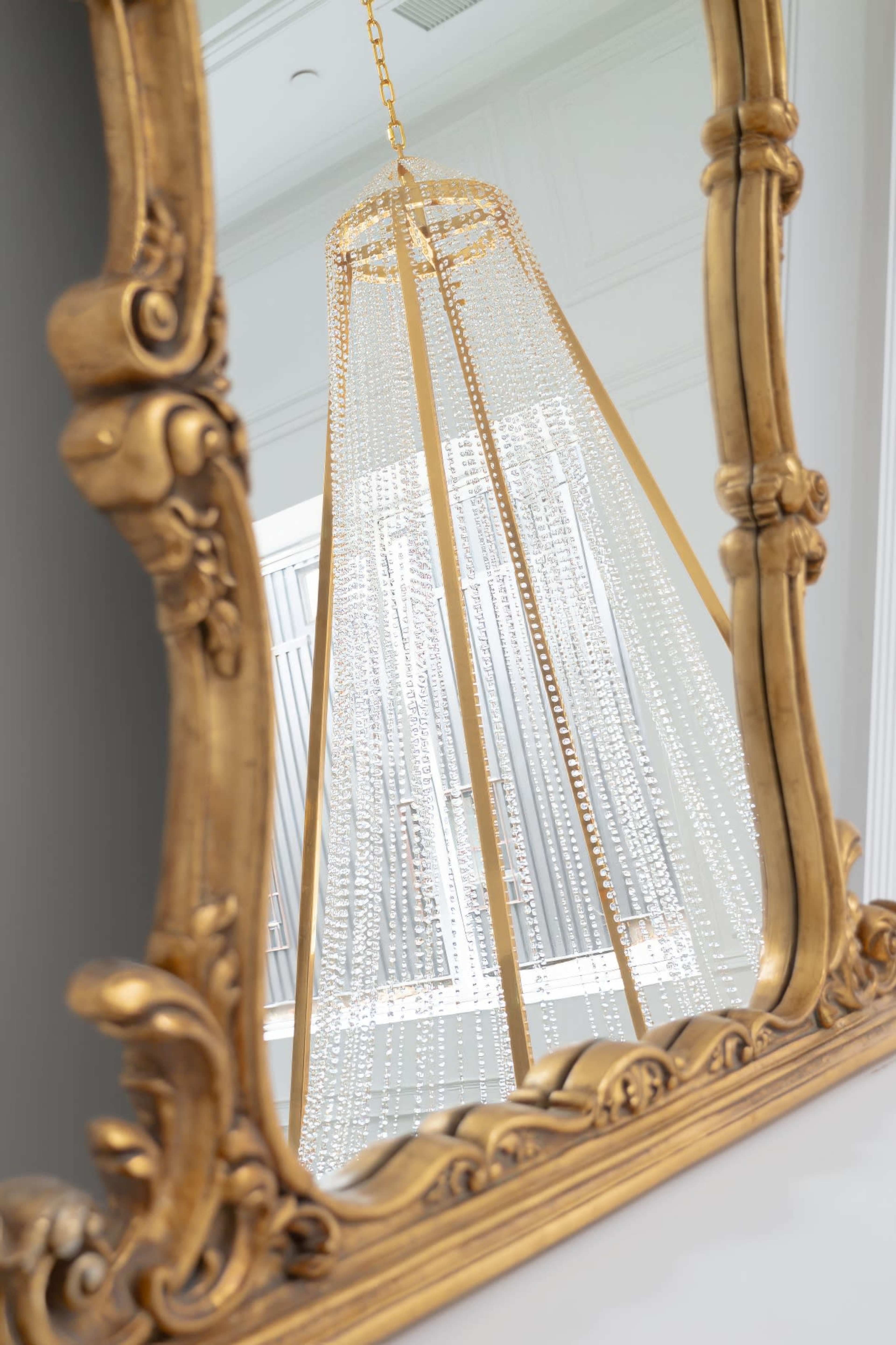 A gold-framed mirror reflects a chandelier made of strands of clear beads.