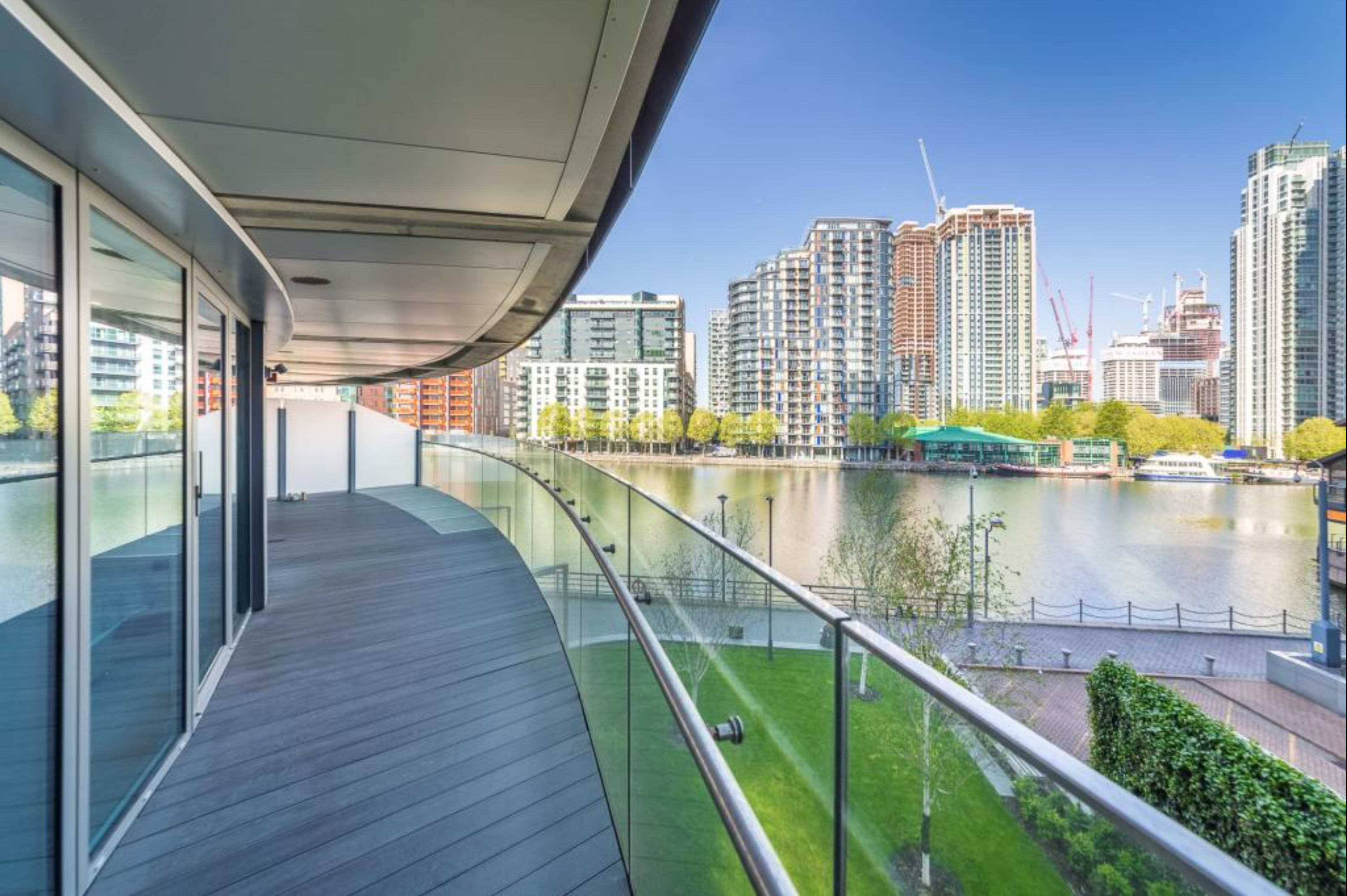 The image shows a modern balcony overlooking a river with tall buildings and construction cranes in the background.