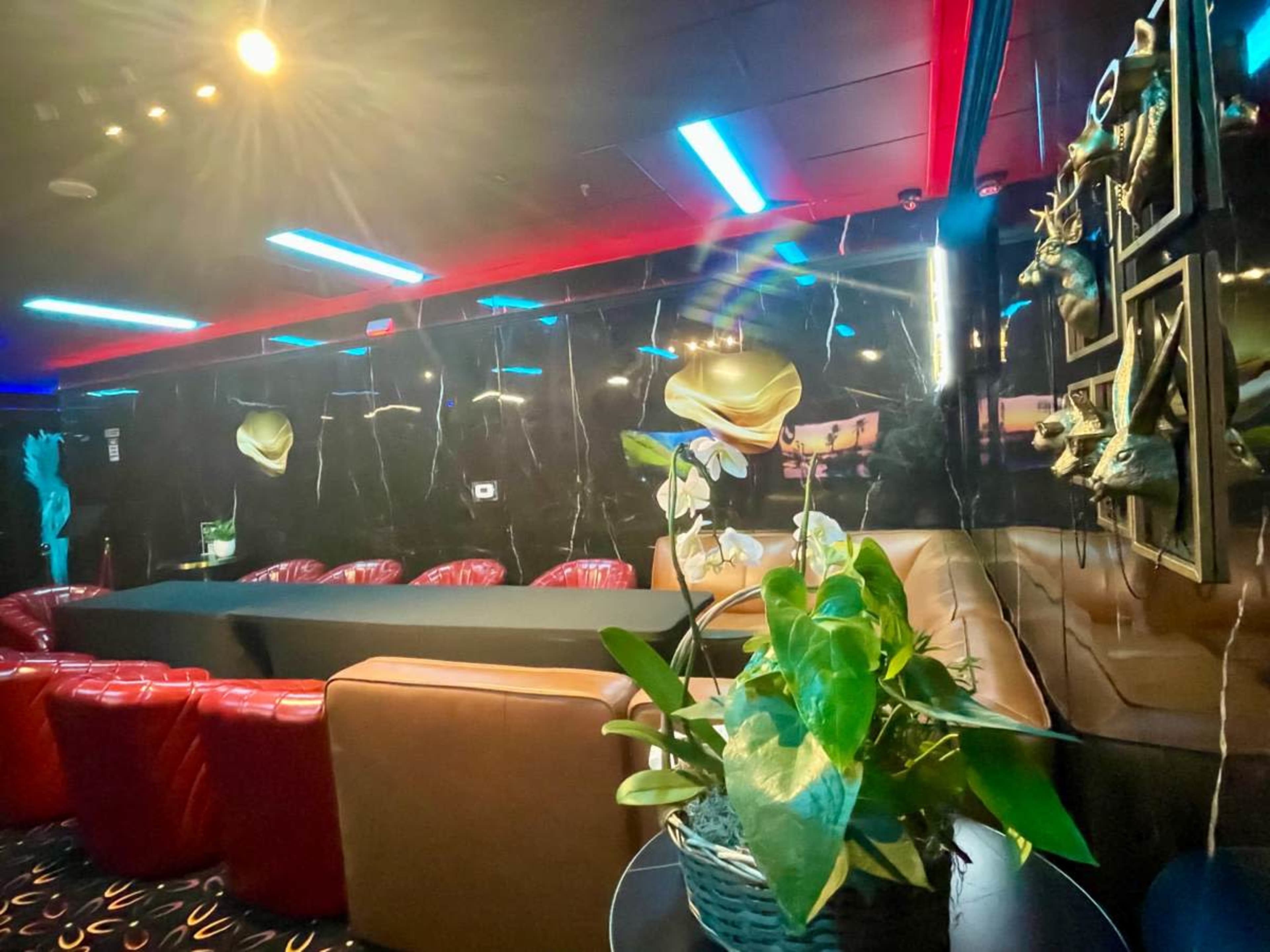 The image shows a modern lounge area with red leather seating, a black marble wall, and colorful lighting.