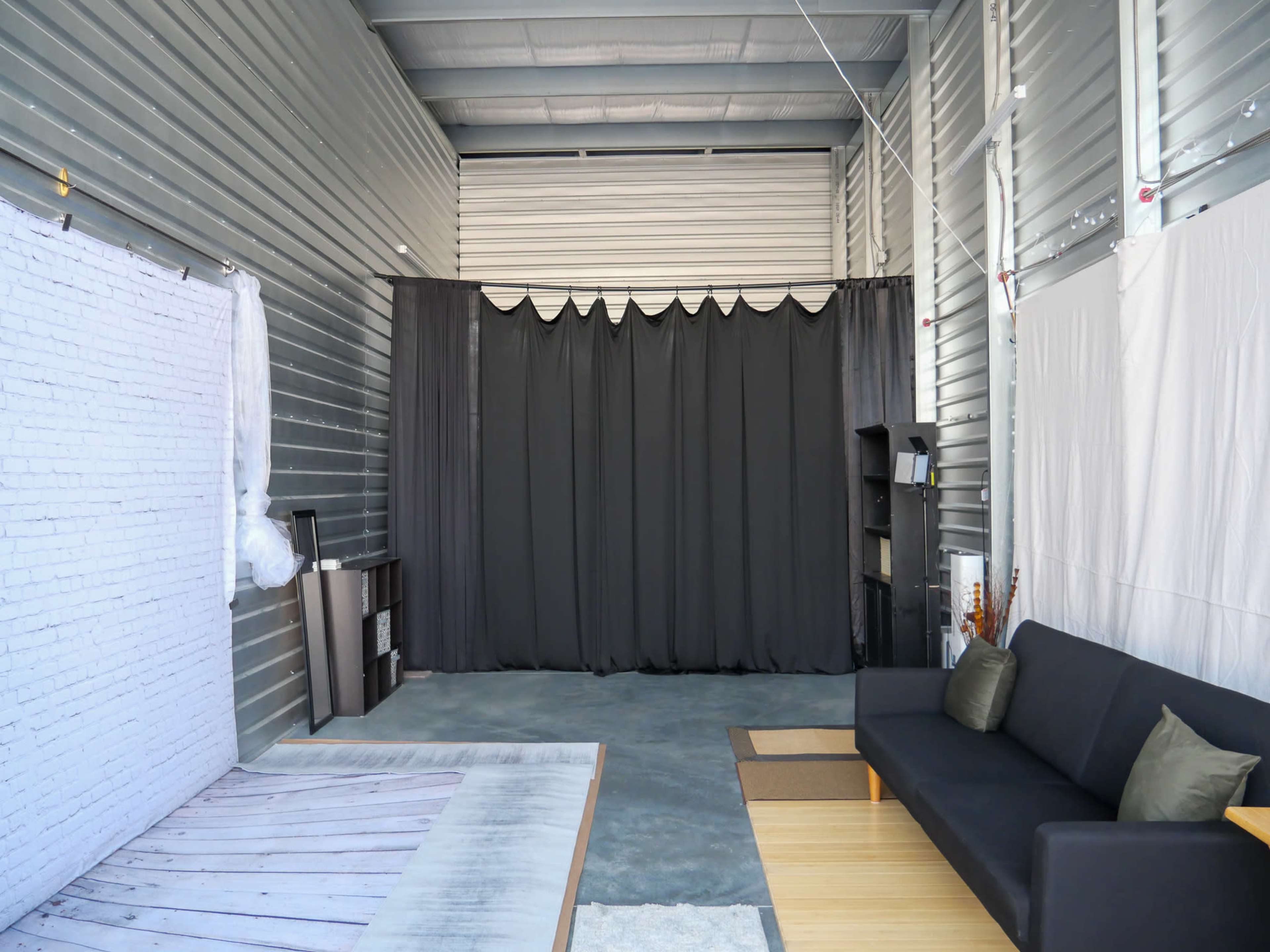 A spacious studio with gray metal walls, featuring a black curtain backdrop and a wooden floor area, along with a black sofa and minimalist decor.