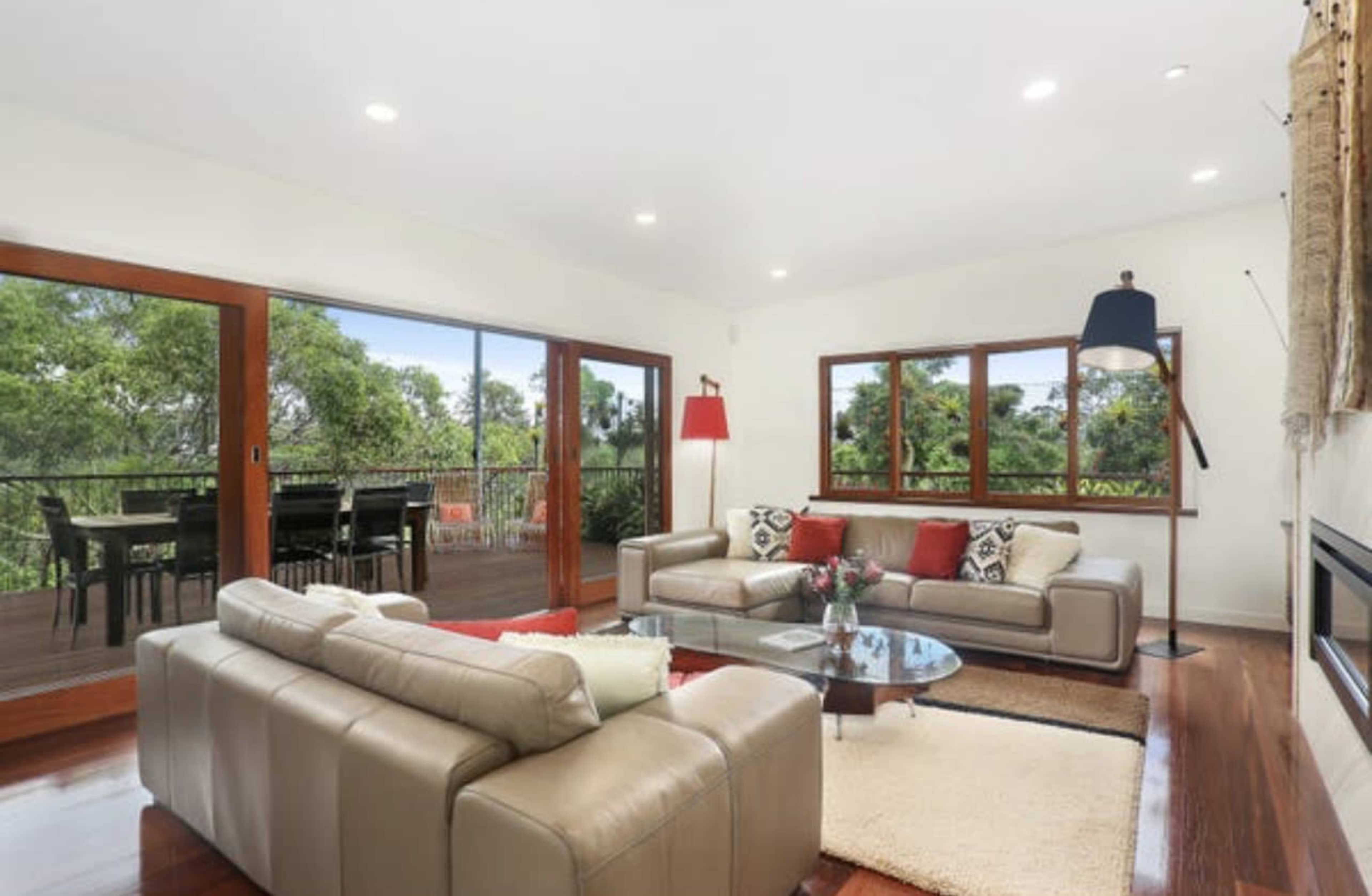 A modern living room features beige leather sofas and large windows overlooking a green landscape.