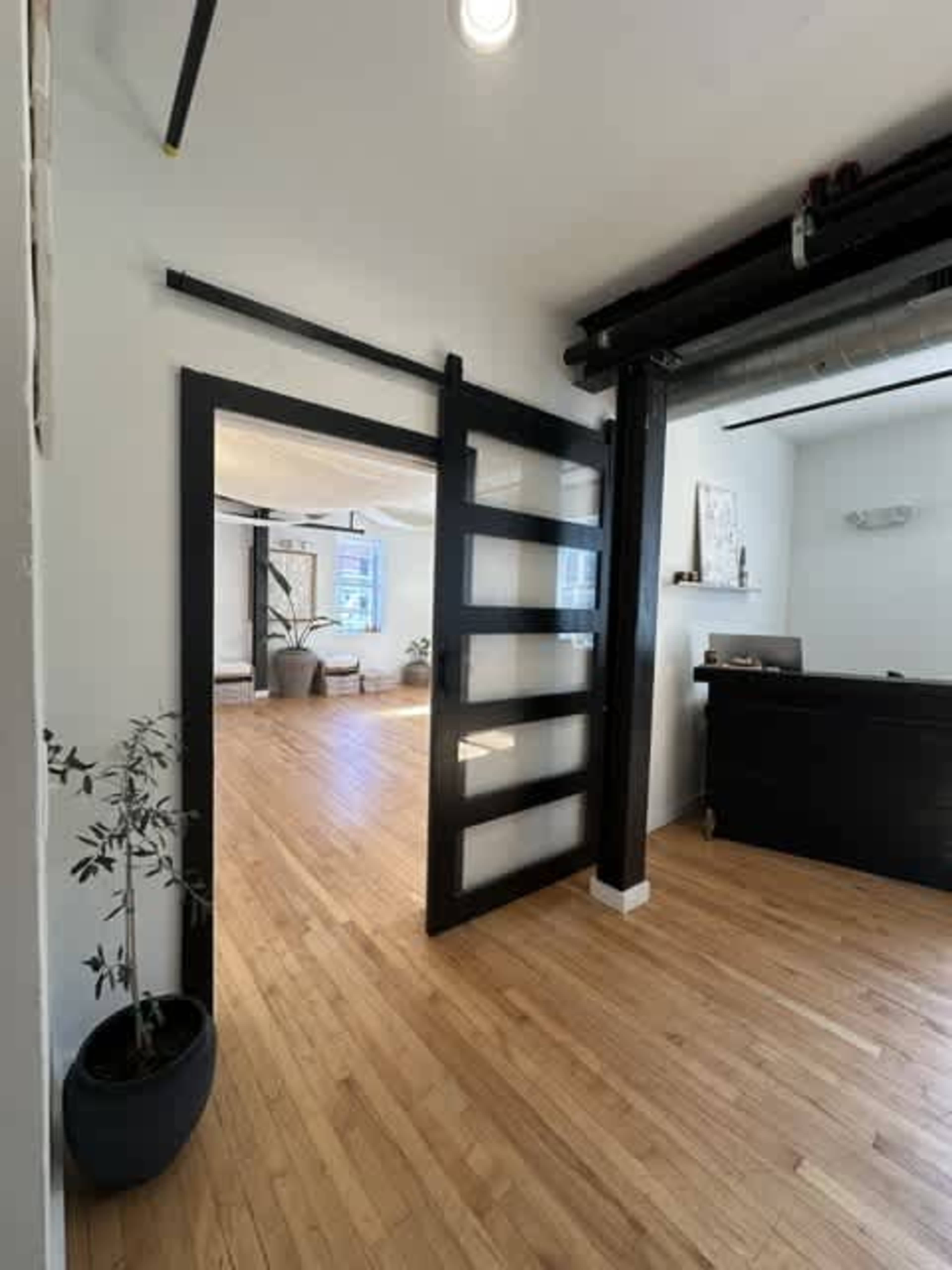 The image shows a modern interior entrance featuring a sliding barn door, hardwood floors, and a reception area with minimal furnishings.