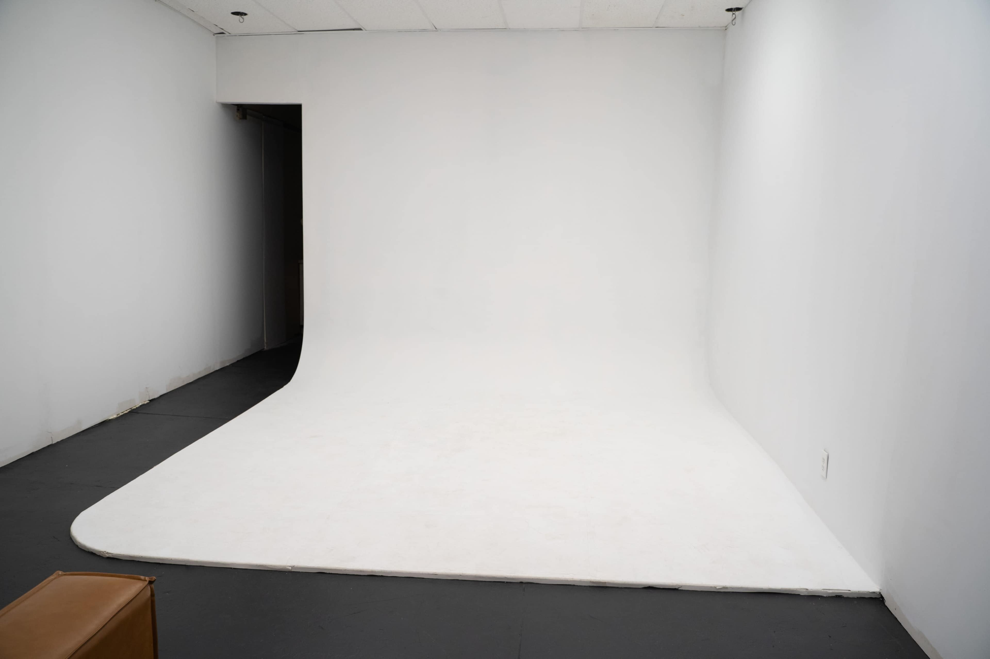 The image shows an empty studio room with a seamless white backdrop and a dark floor.