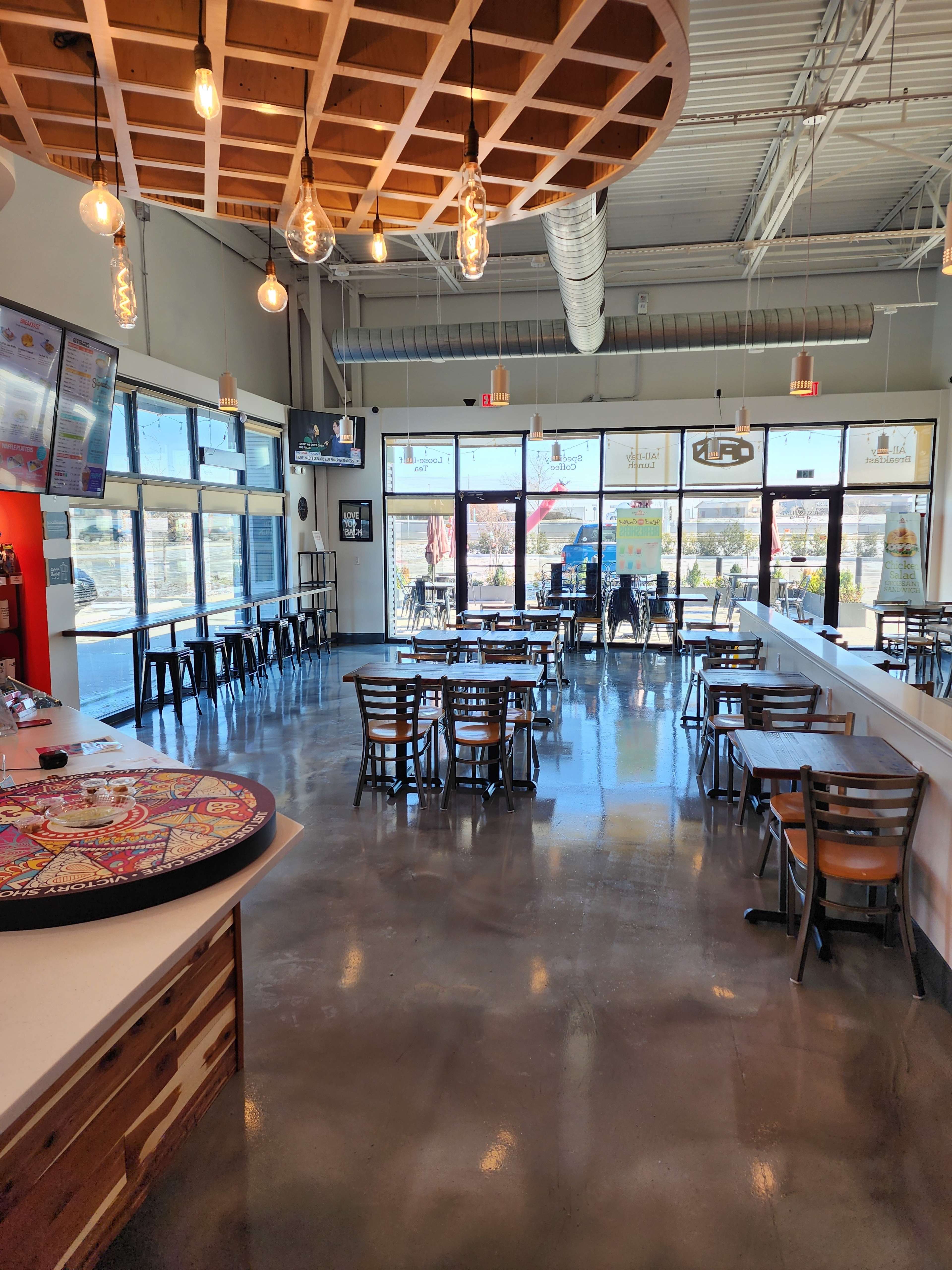 A modern dining space with large windows, polished concrete floors, and a mix of tables and chairs arranged for customers.