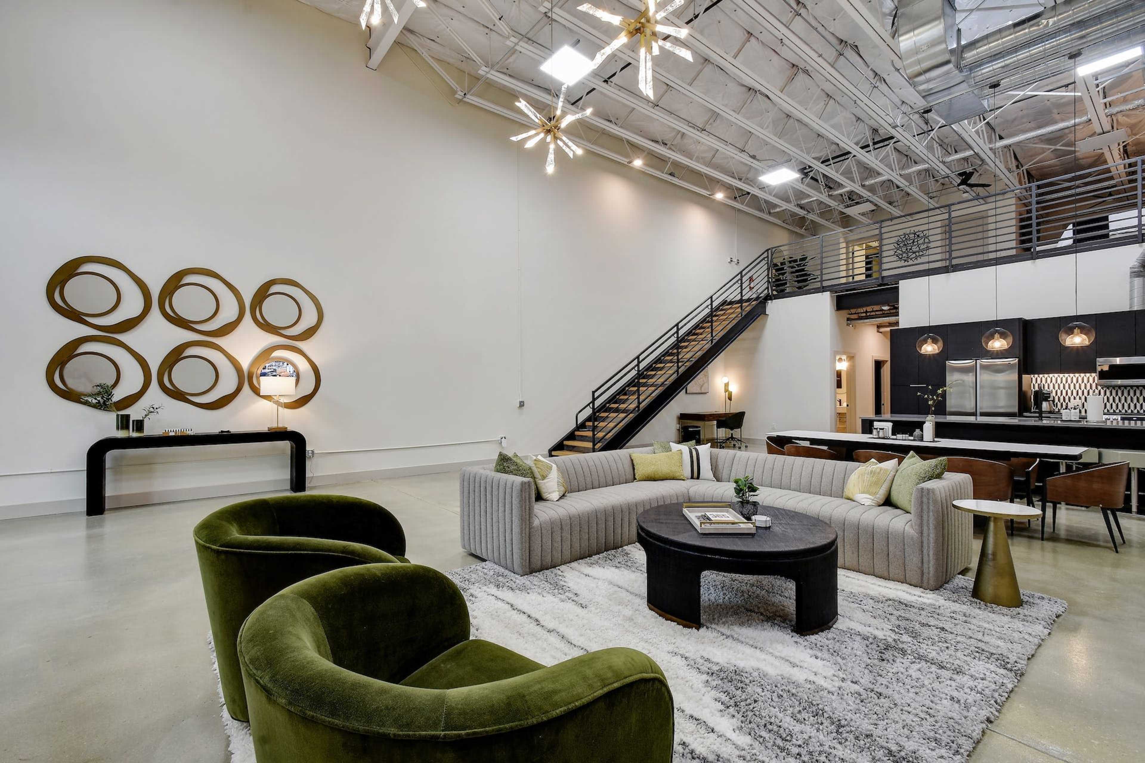 A spacious modern living area with a large sectional sofa, a round coffee table, and a staircase leading to a lofted area.