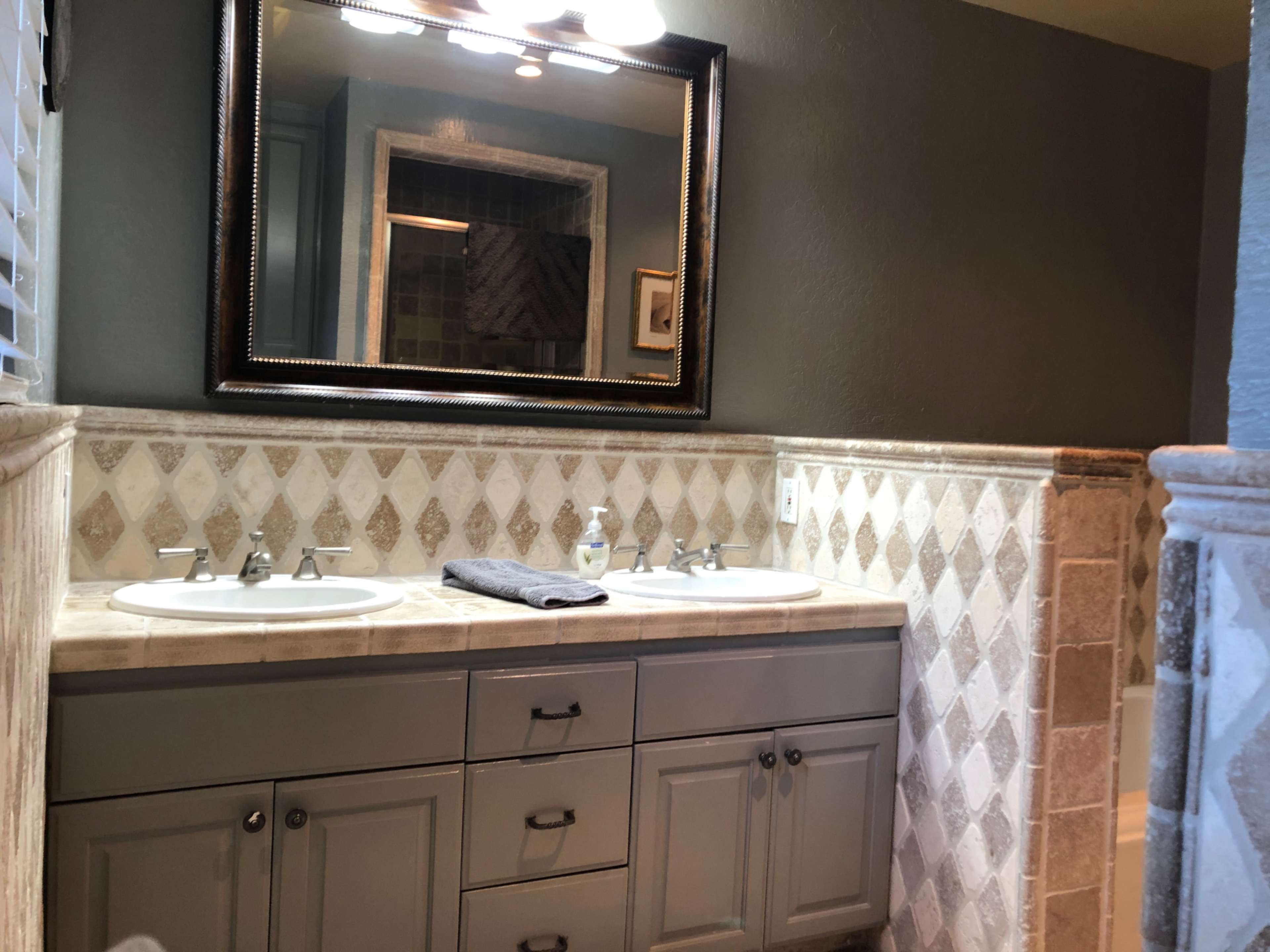 A bathroom with dual sinks, a mirrored cabinet above, and tiled walls featuring a diamond pattern.