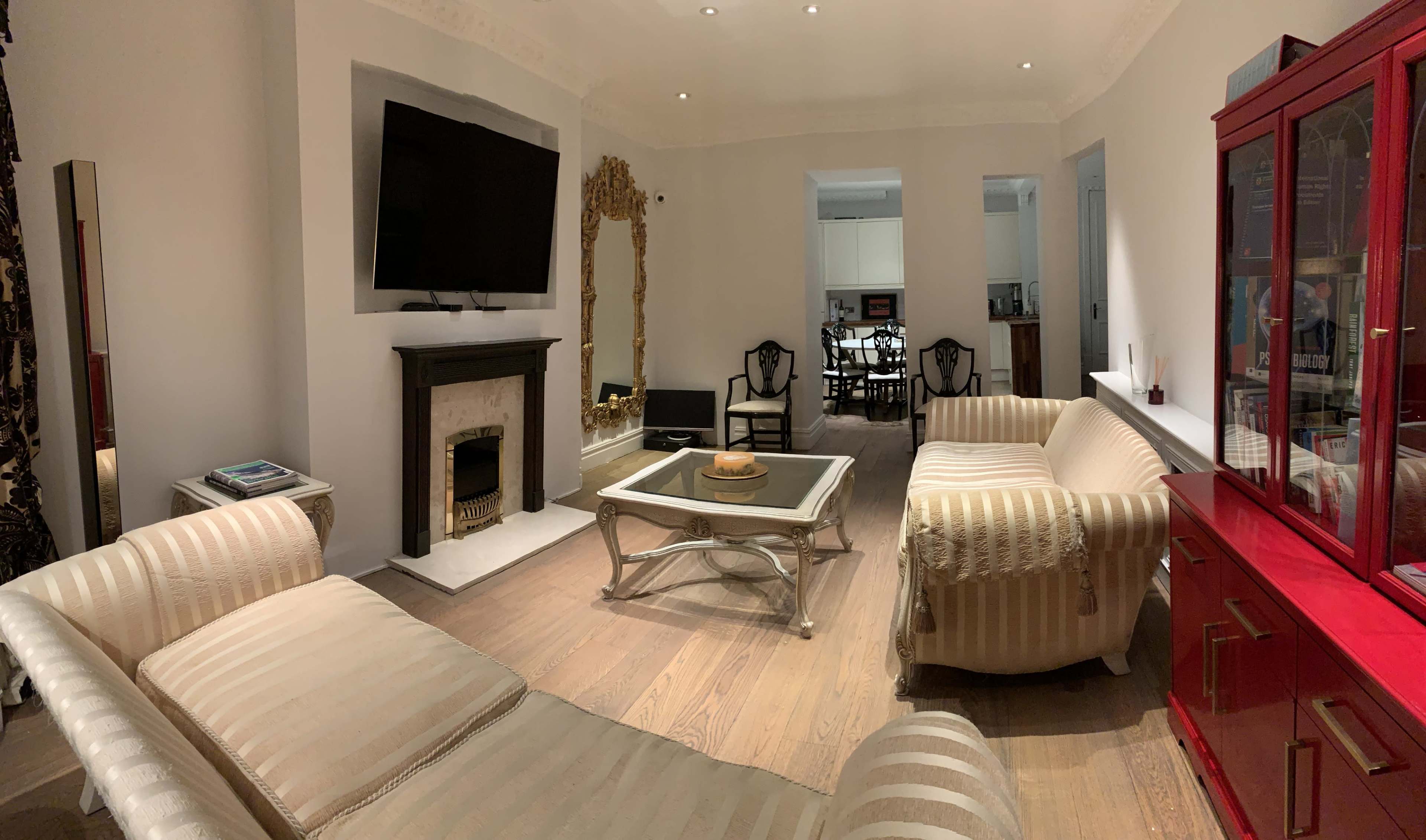 The image shows a modern living room with a large mirror, flat-screen TV, and two sofas arranged around a coffee table.