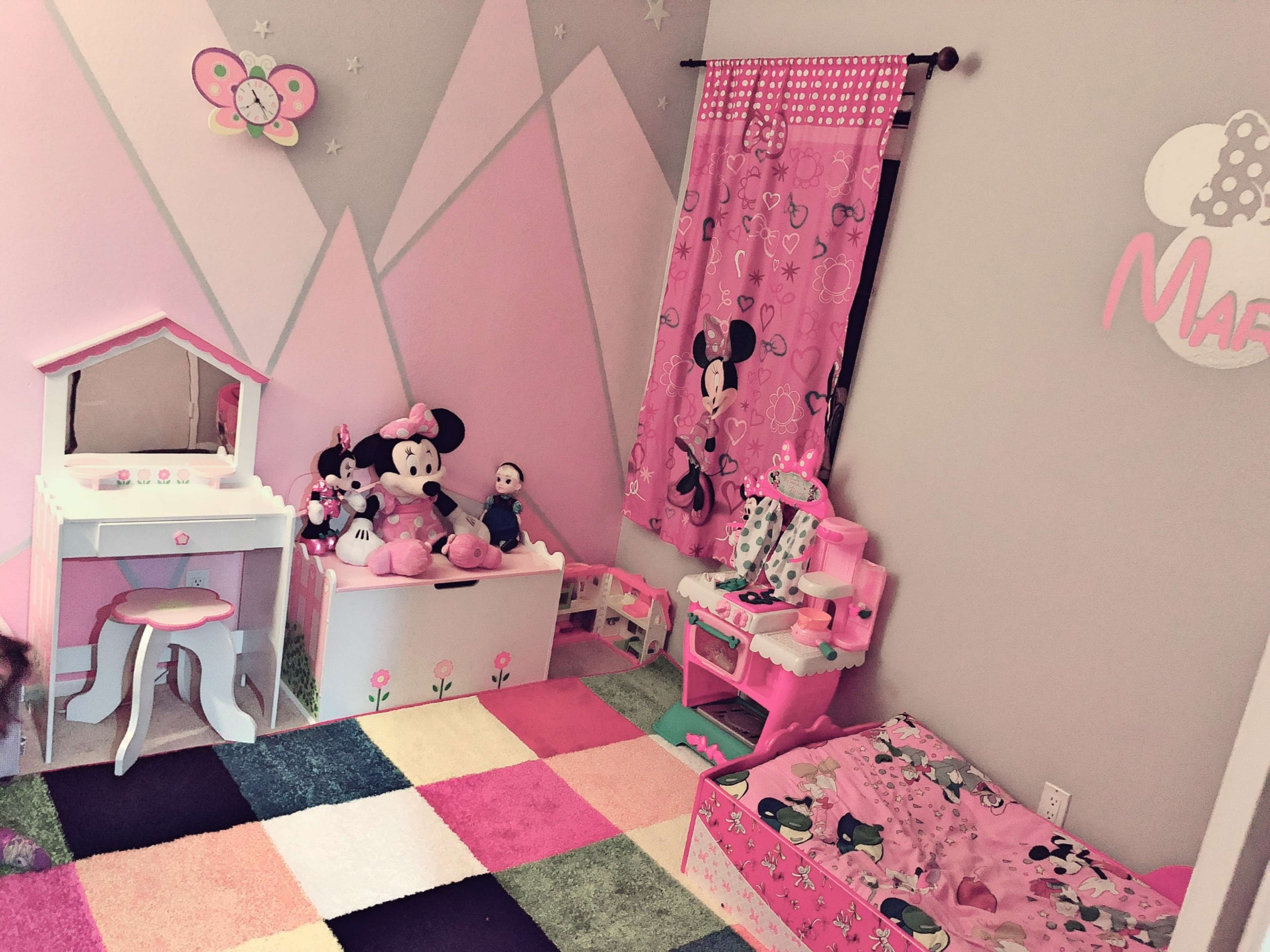 A children's bedroom decorated in pink with a variety of Minnie Mouse-themed items, including a bed, a vanity, and stuffed toys.