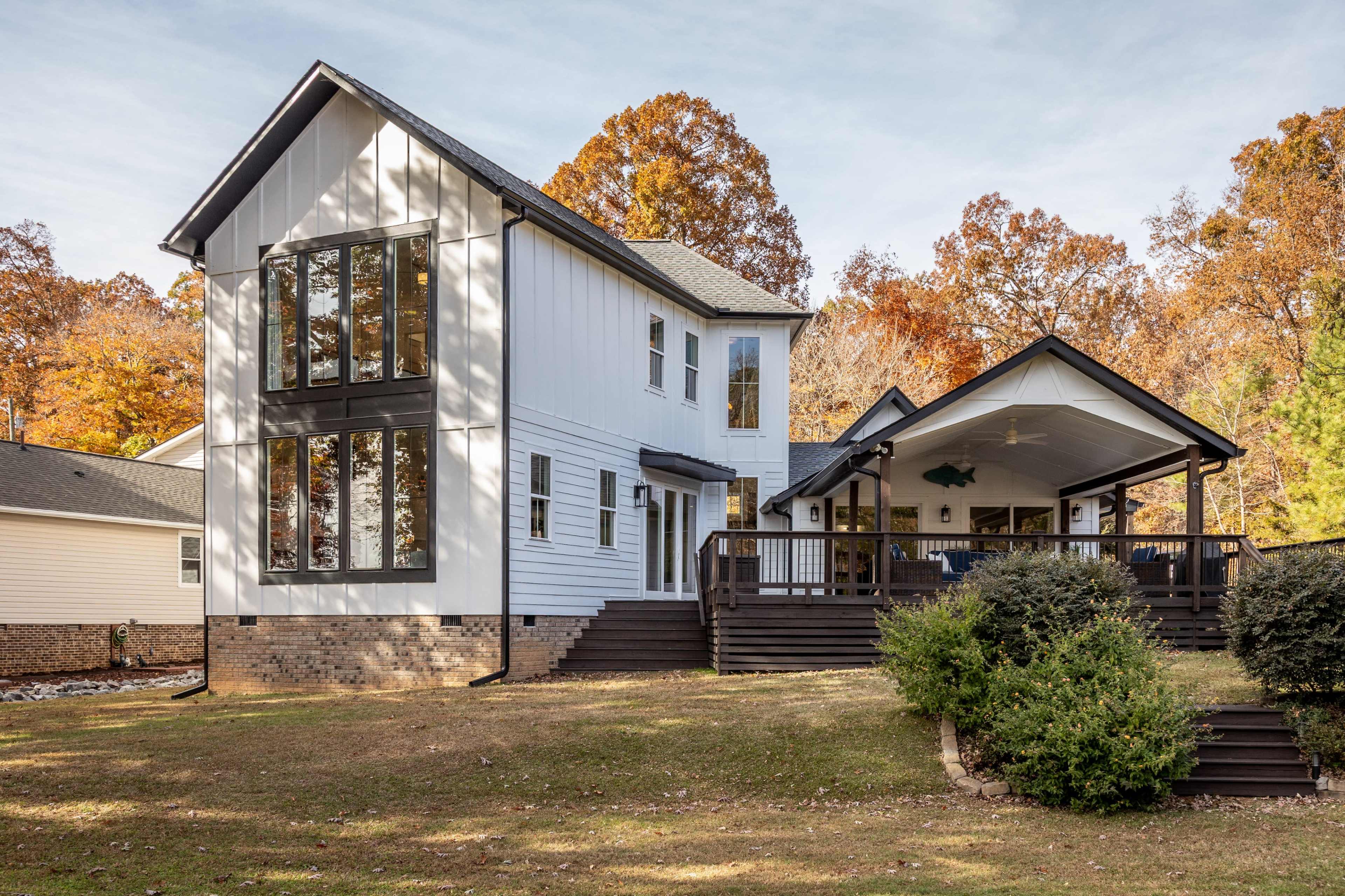 A two-story house with a large porch and multiple windows is surrounded by trees showcasing autumn foliage.