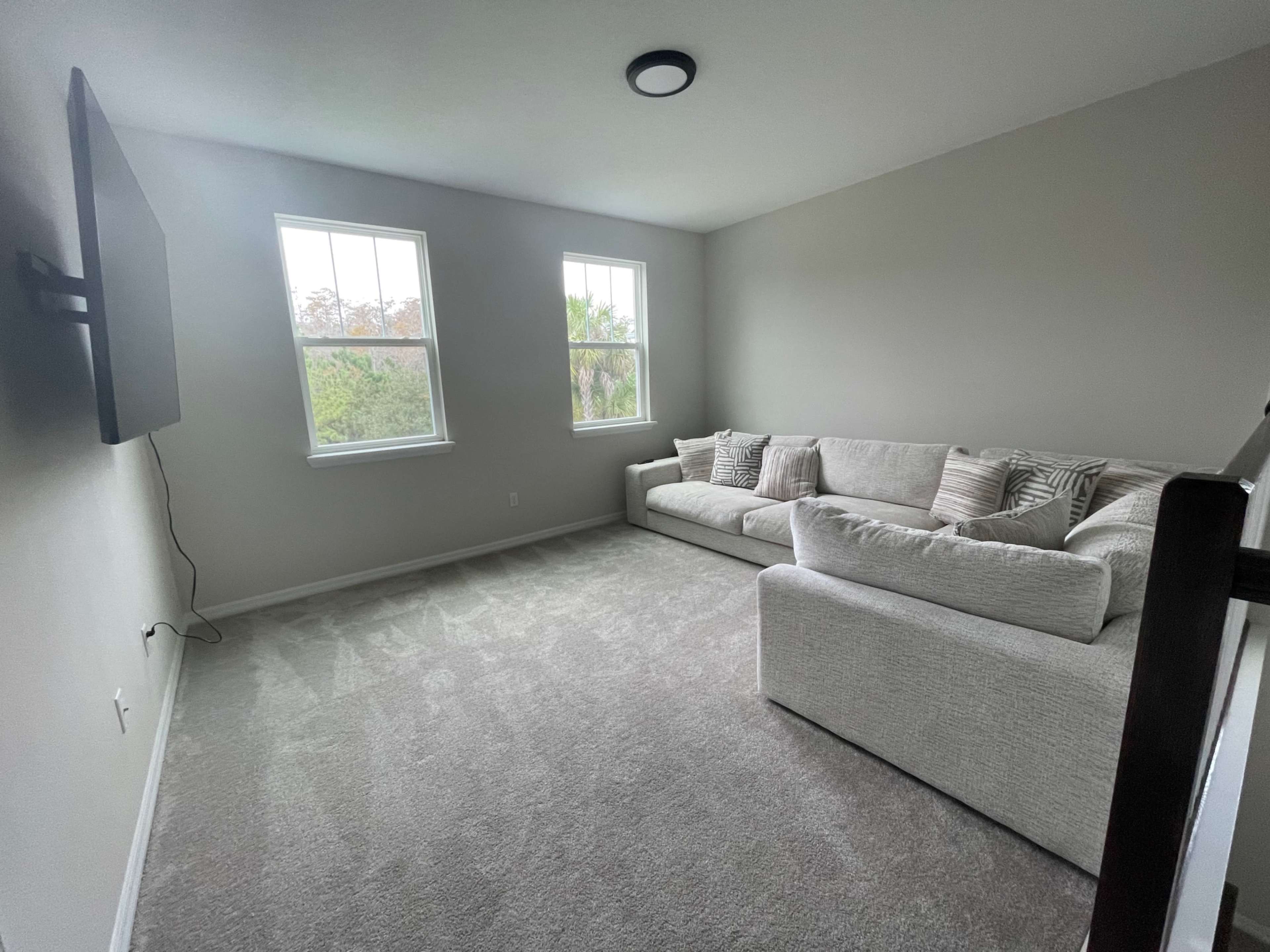 A light-filled living room features a large, plush sectional sofa and two windows overlooking greenery.