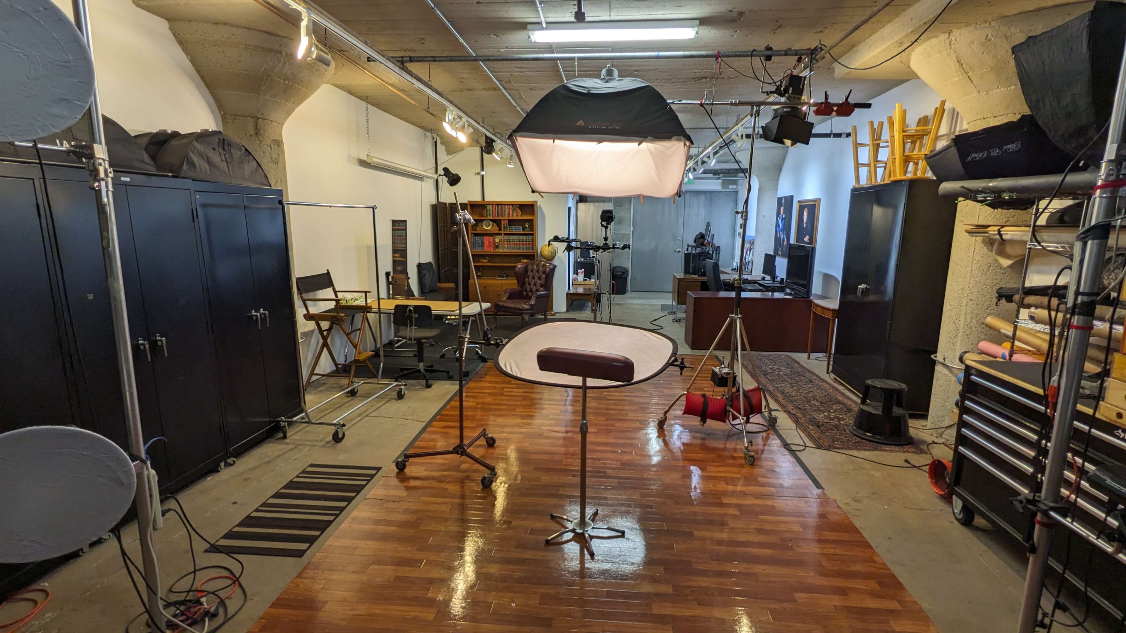 The image shows a photography studio equipped with various lighting equipment, a backdrop stand, and a wooden floor.