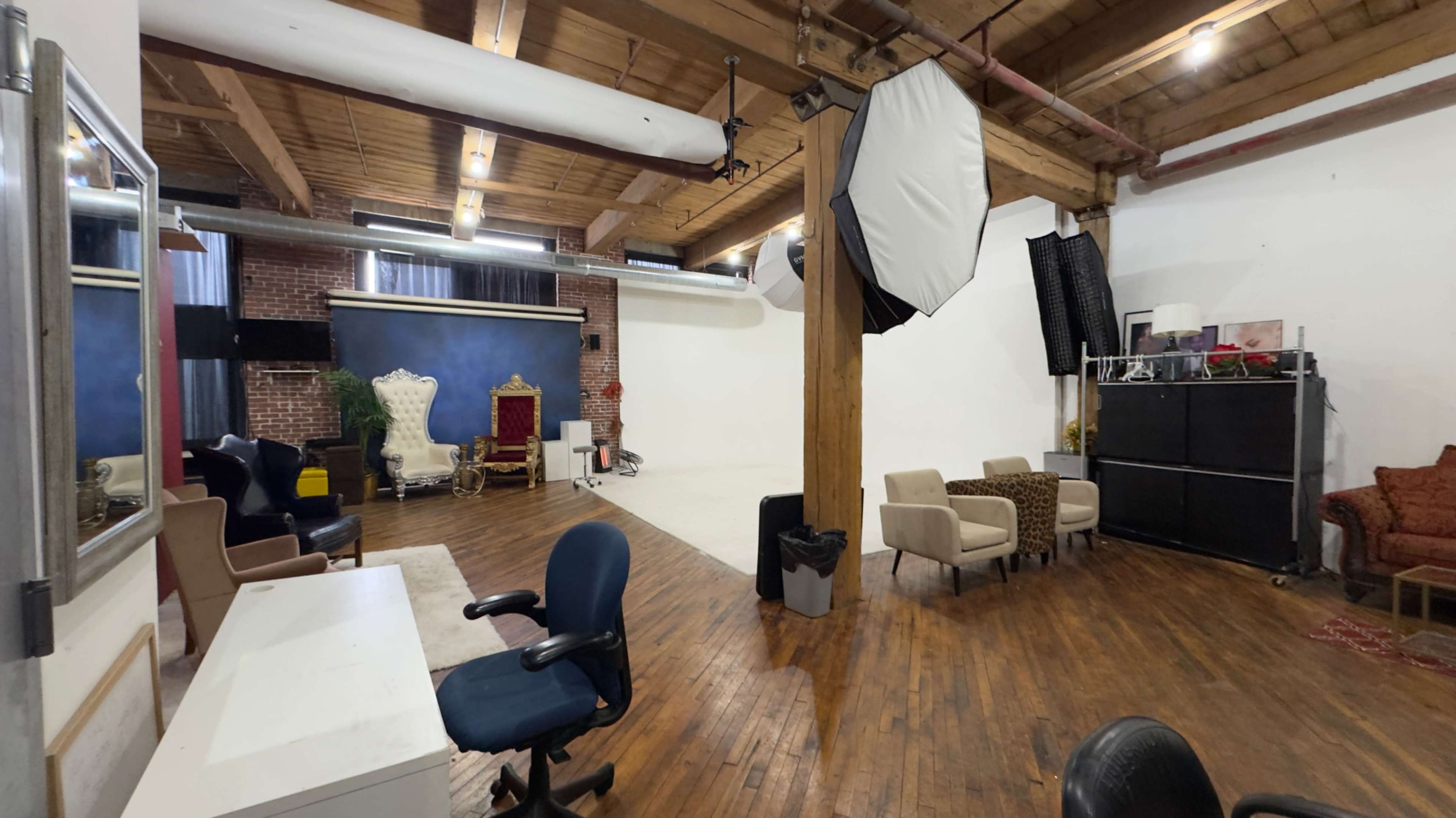 A spacious photo studio features wooden floors, various seating options, a backdrop area, and professional lighting equipment.