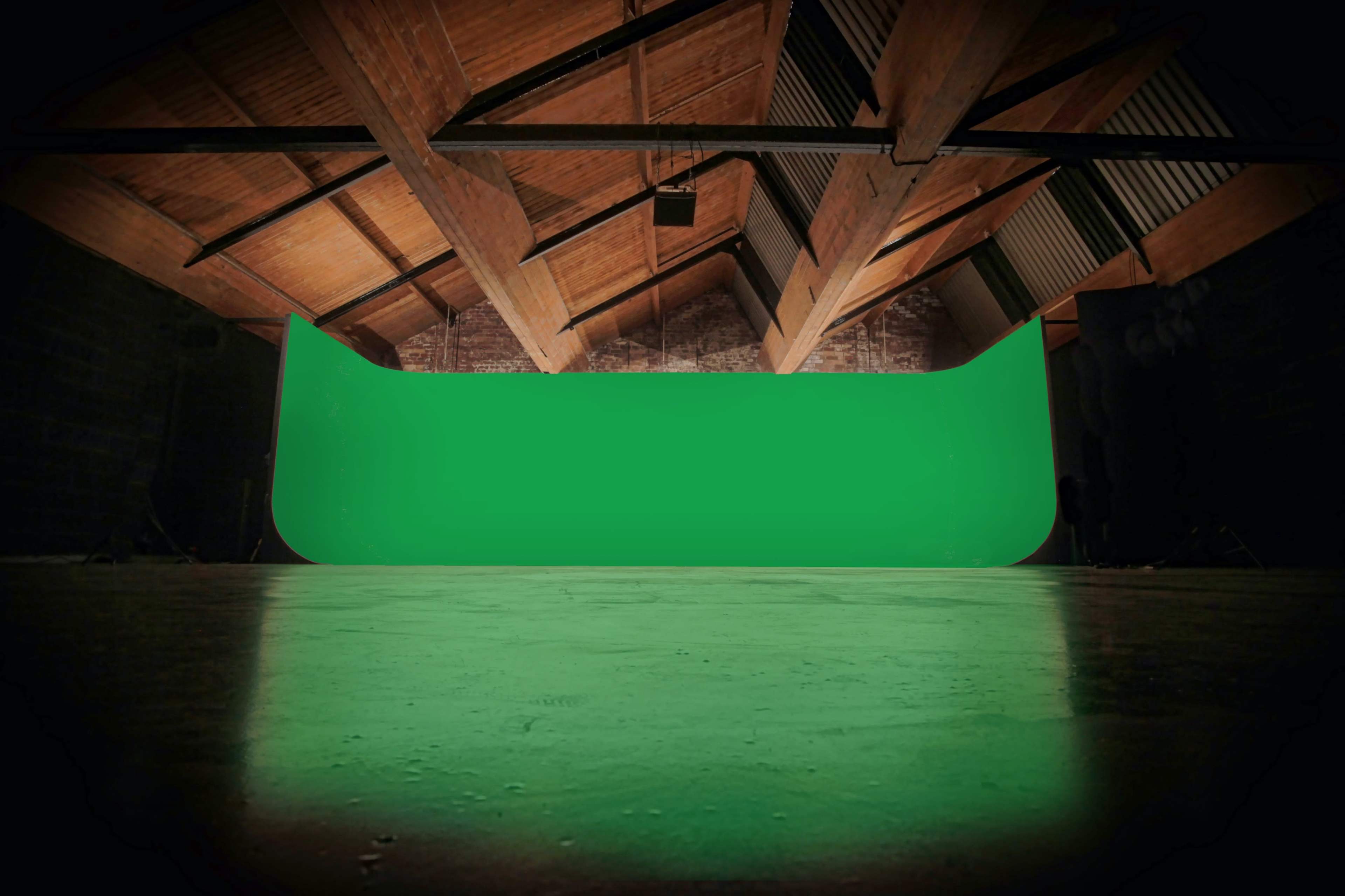 An indoor studio space with a curved green backdrop and wooden beams overhead.