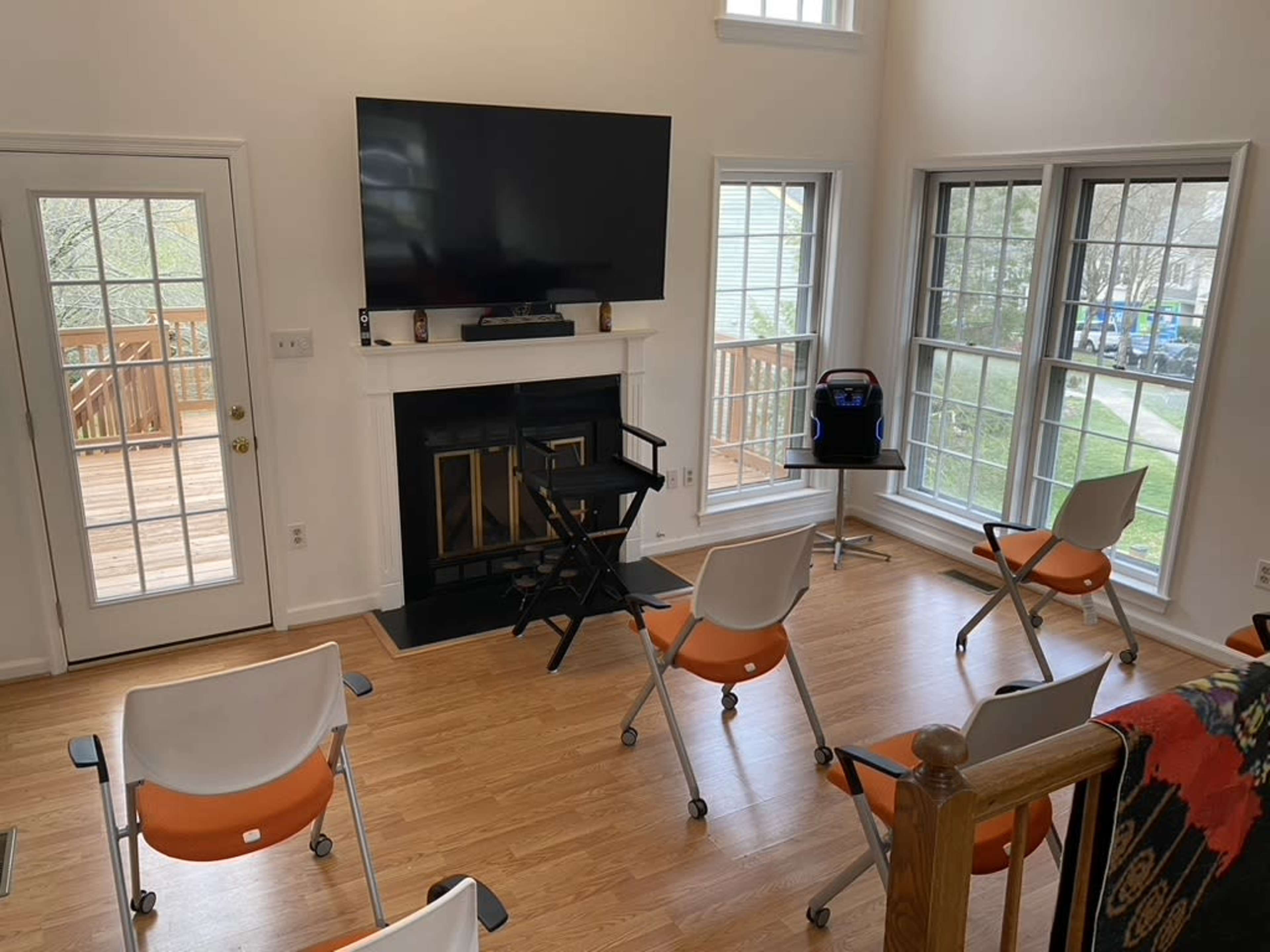 A spacious room with a television mounted above a fireplace, surrounded by chairs arranged in a semi-circle.