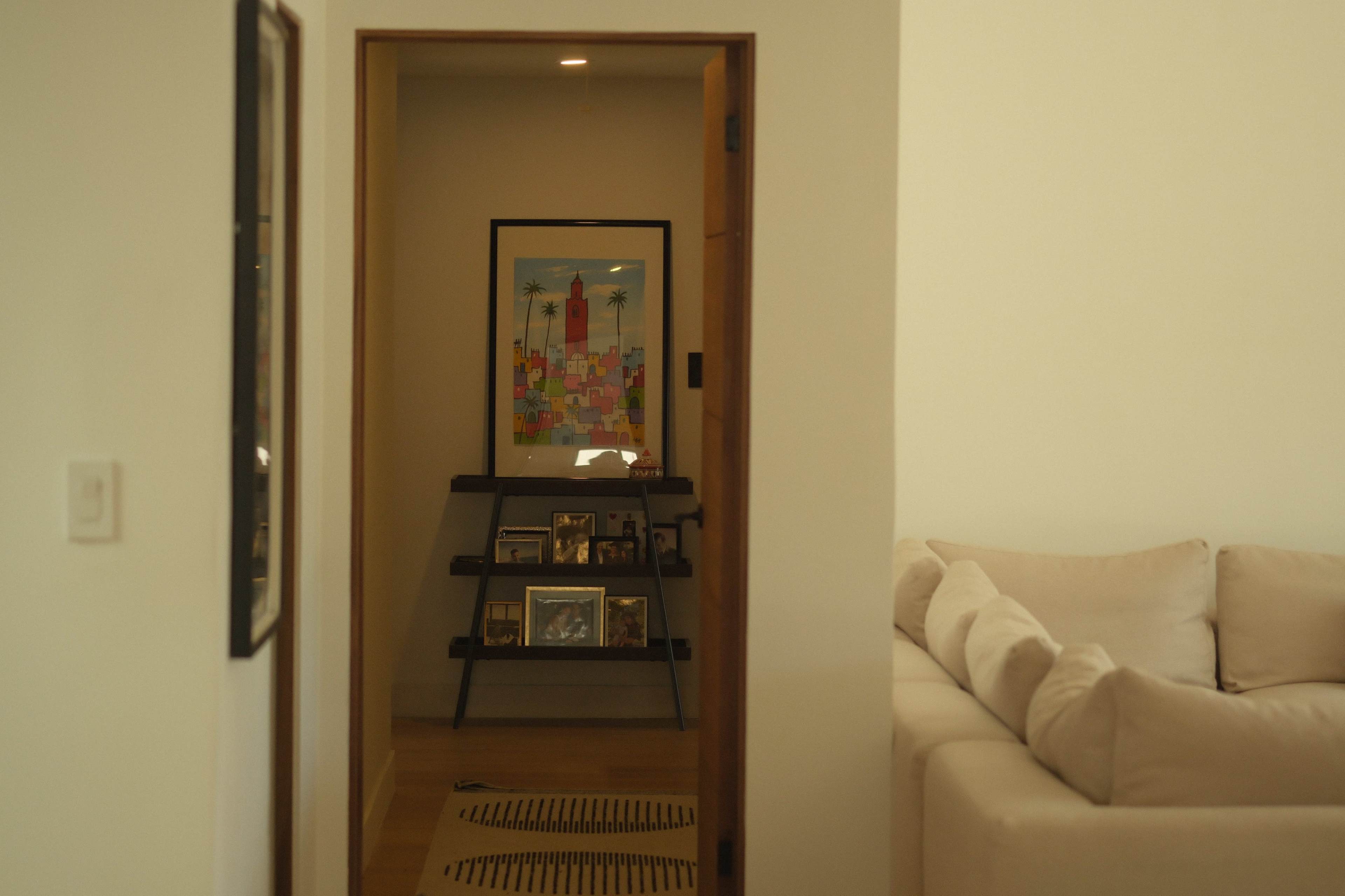 A hallway leads to a small display shelf with framed photos and artwork in a softly lit room.