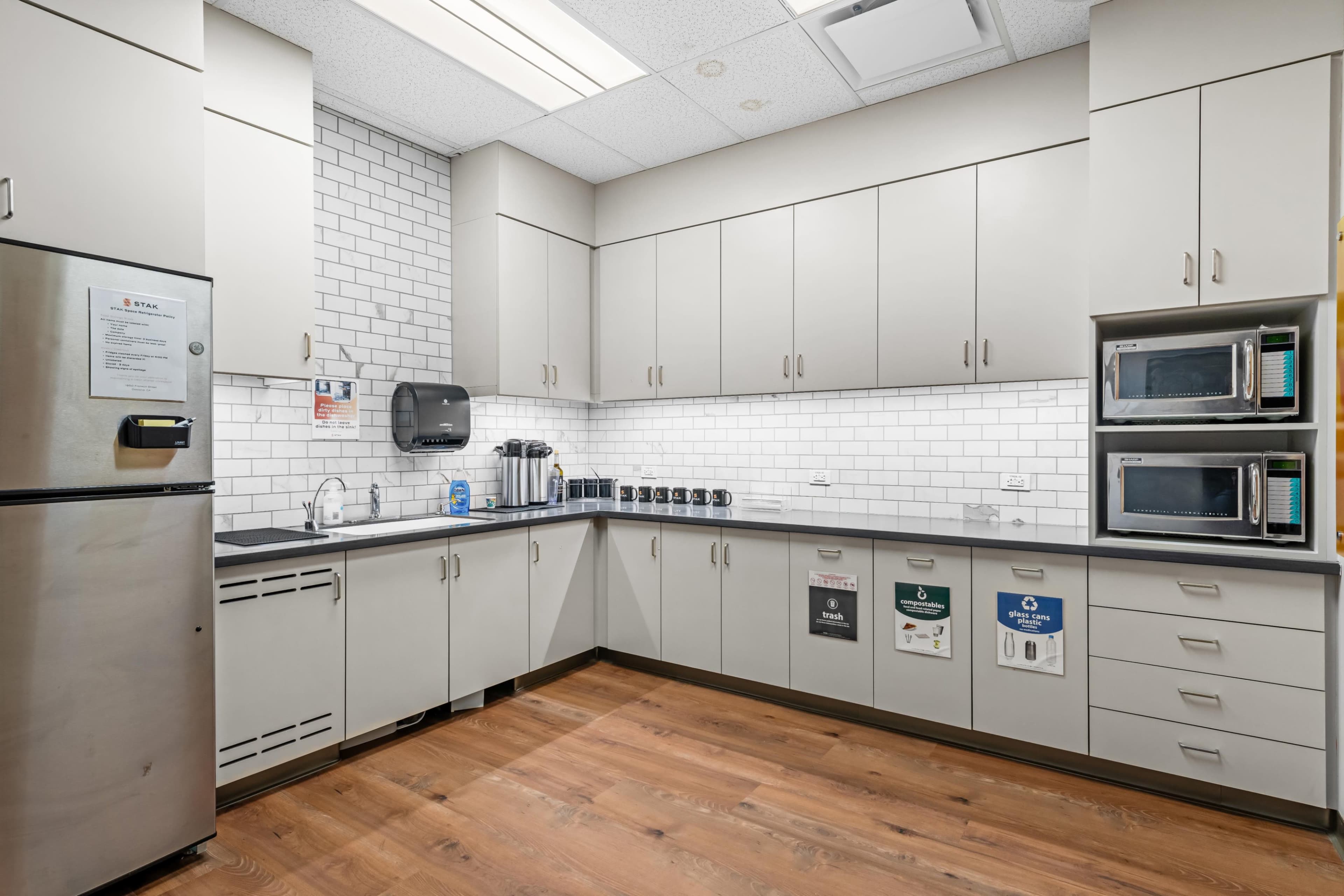 The image shows a modern kitchen with light grey cabinets, white subway tile backsplash, stainless steel appliances, and a wooden floor.