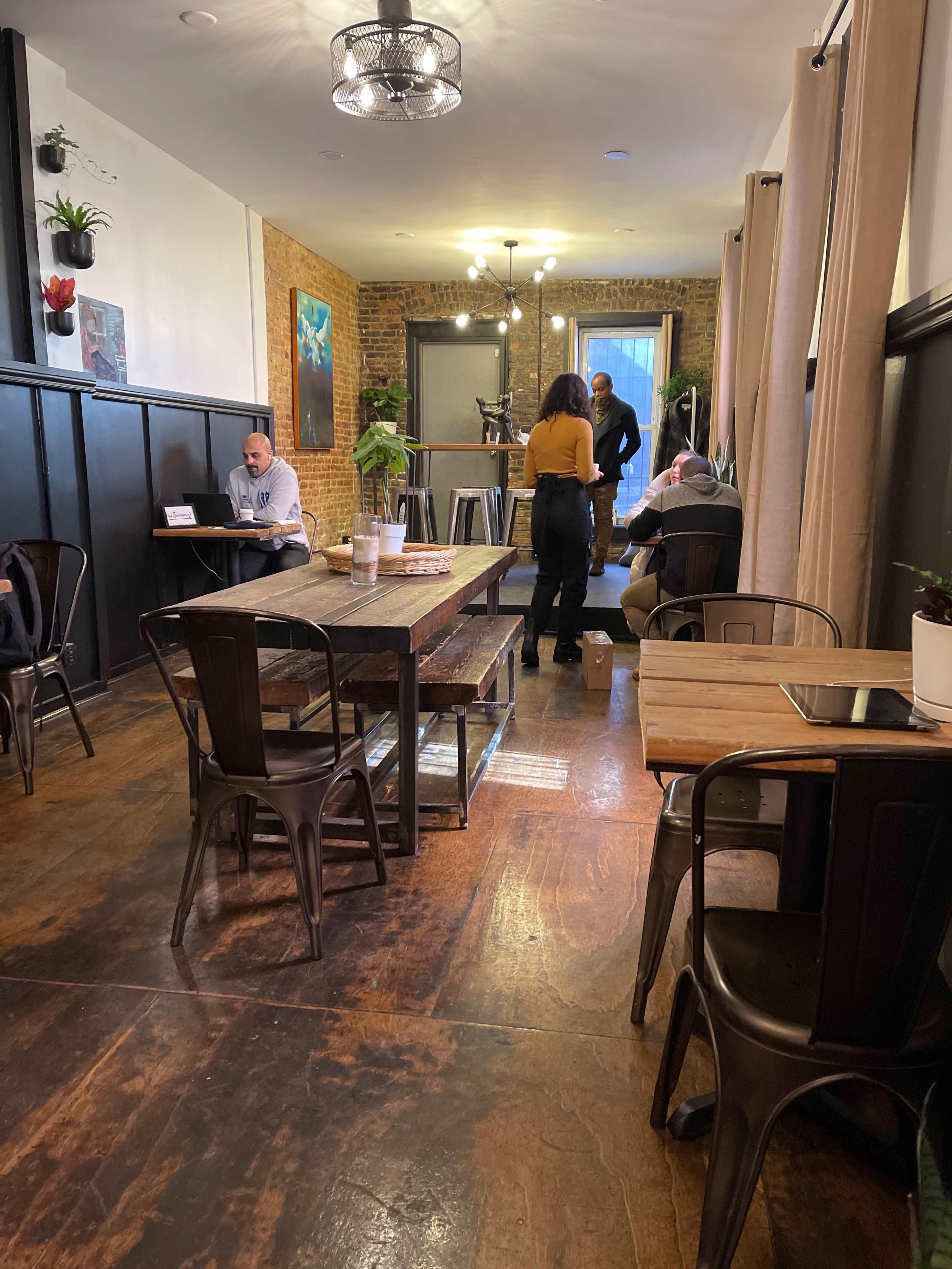 A cozy café interior with wooden tables, metal chairs, and patrons engaged in various activities, including working on laptops and conversing.