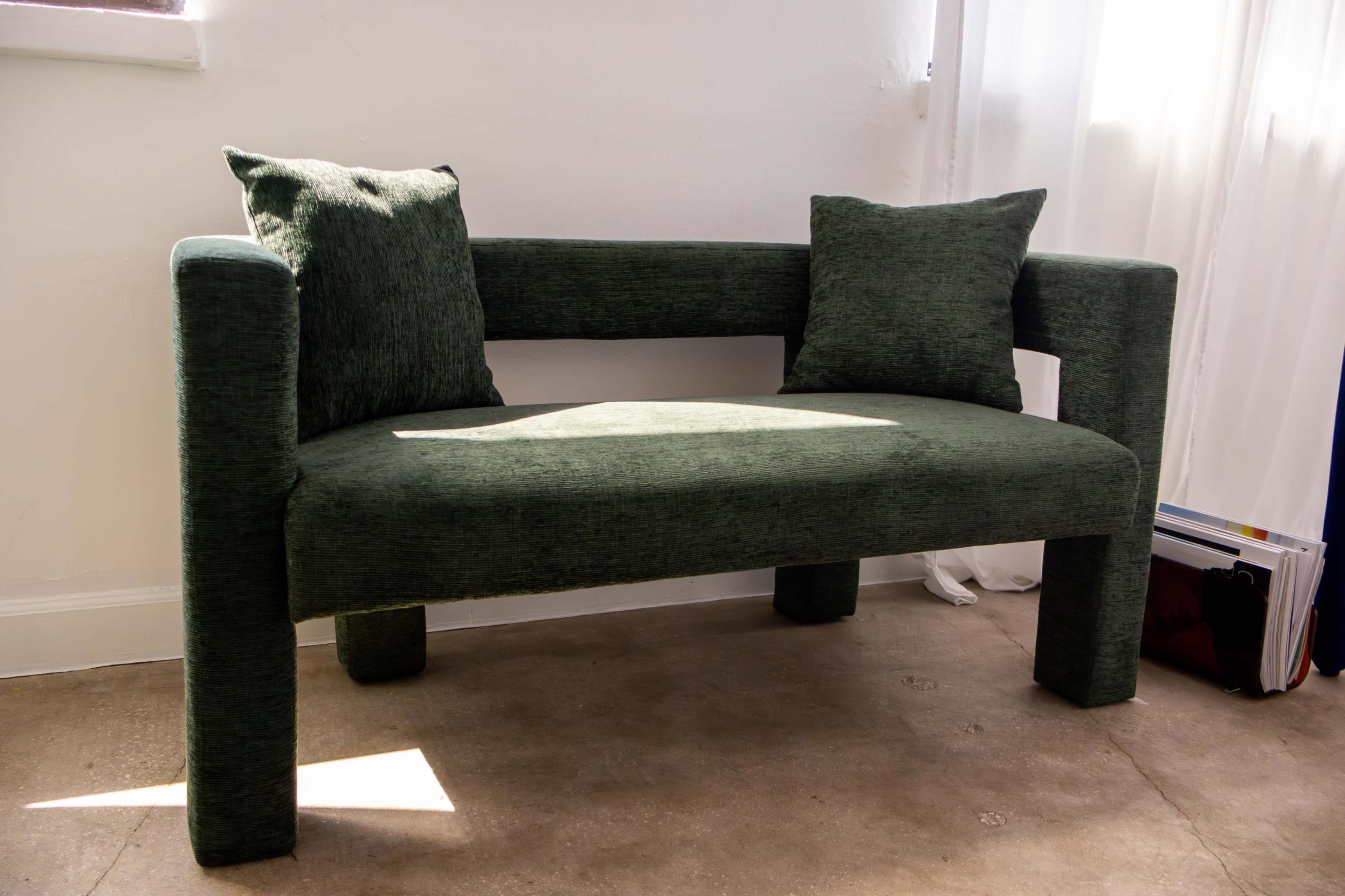 A green upholstered bench with two matching cushions is positioned near a window.