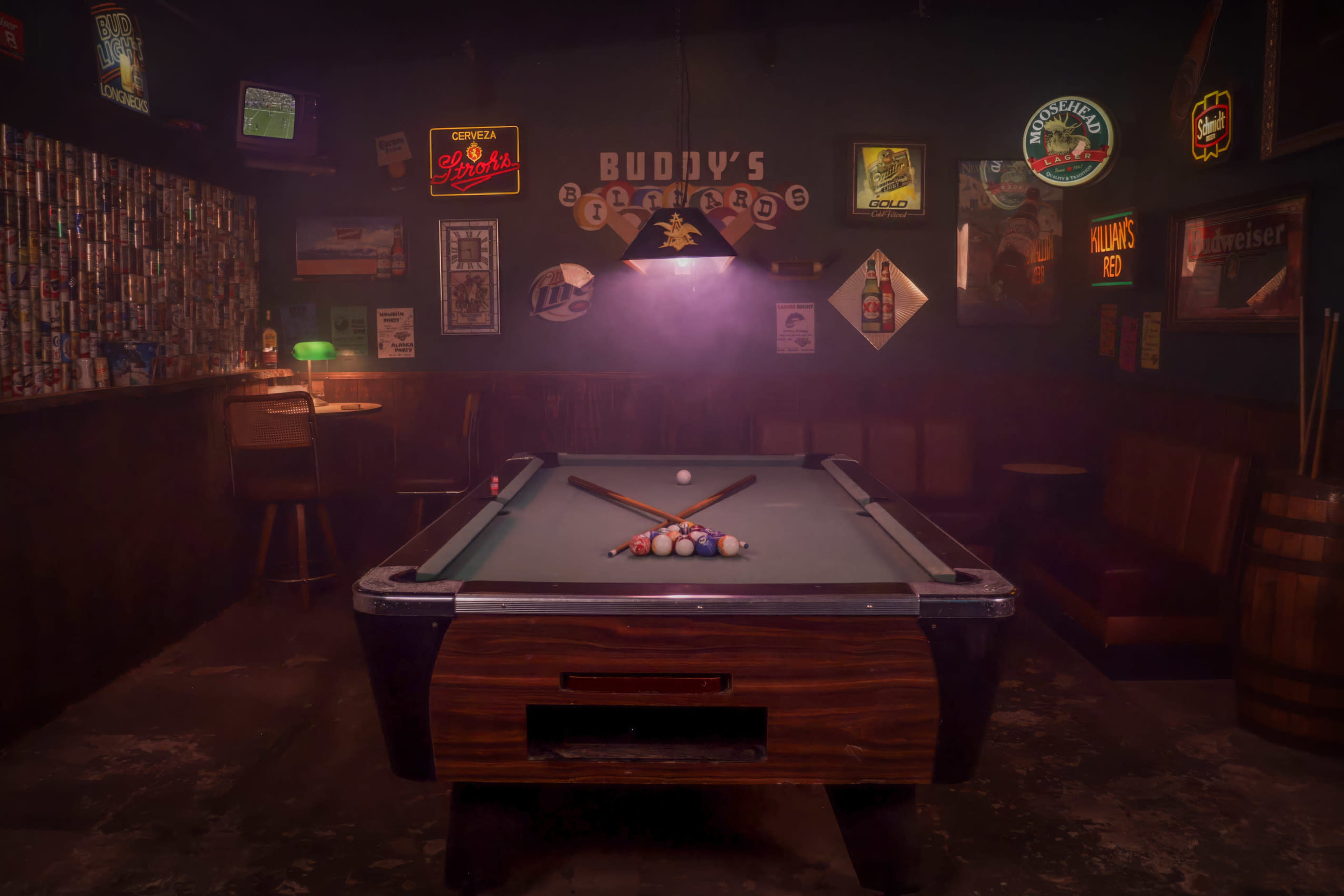 The image shows a dimly lit pool room featuring a green billiard table with a cue stick and a rack of balls, surrounded by vintage bar decor and illuminated by a hanging light.