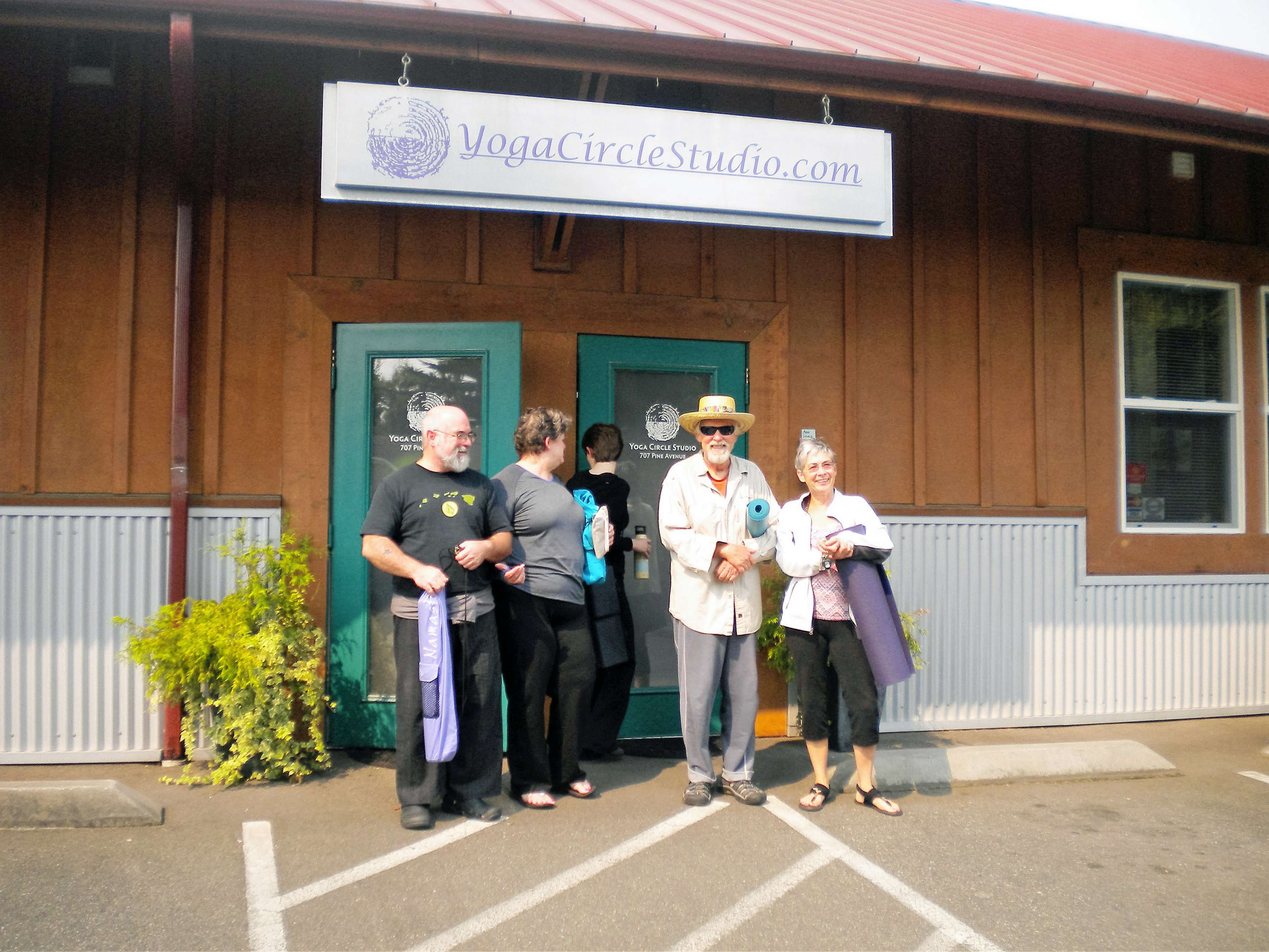 A group of people stand outside a yoga studio, holding yoga mats and prepared for class.