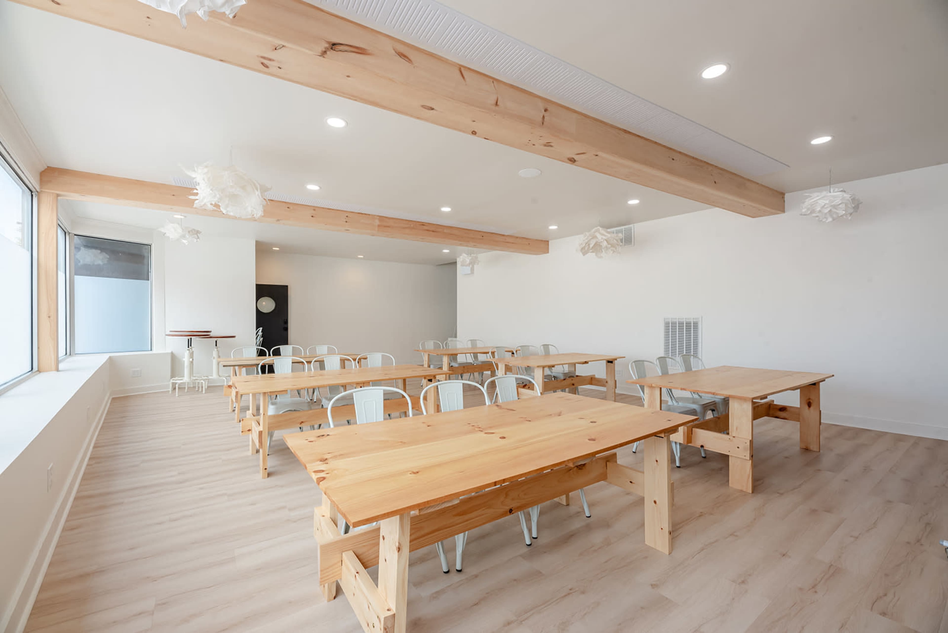 A spacious and brightly lit classroom featuring multiple wooden tables arranged in rows, with metal chairs and modern light fixtures.