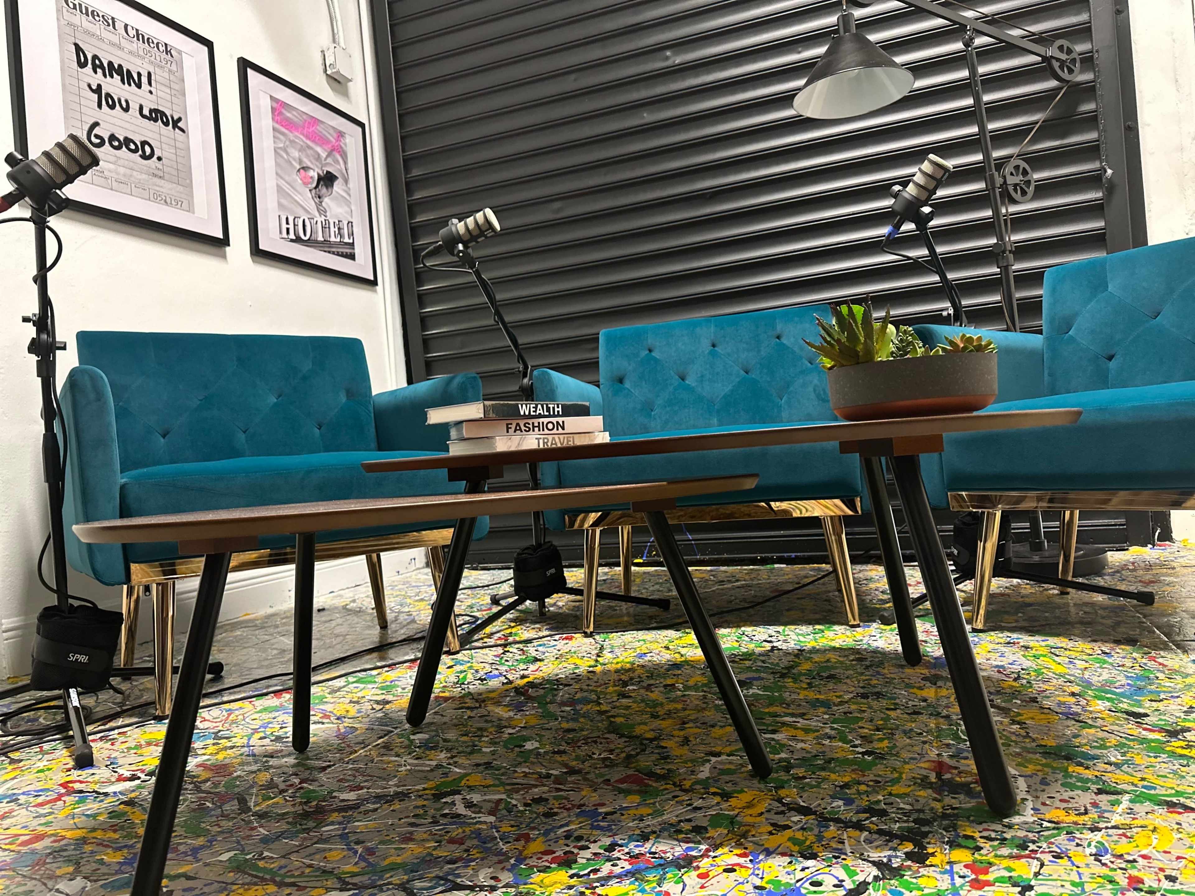 A modern seating area with two vibrant blue chairs, a wooden coffee table, and framed artworks on the wall, set against a closed rolling shutter.
