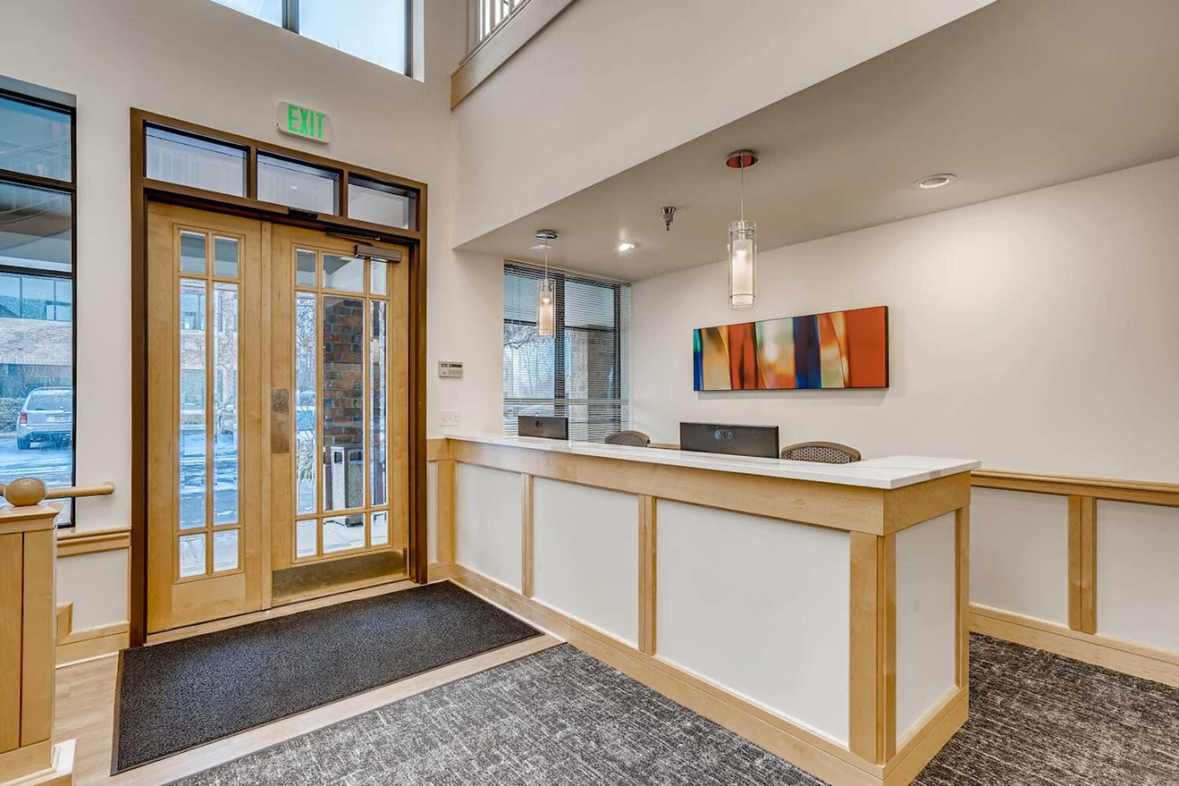 A bright, modern reception area with a front desk, large glass doors, and a colorful artwork piece on the wall.