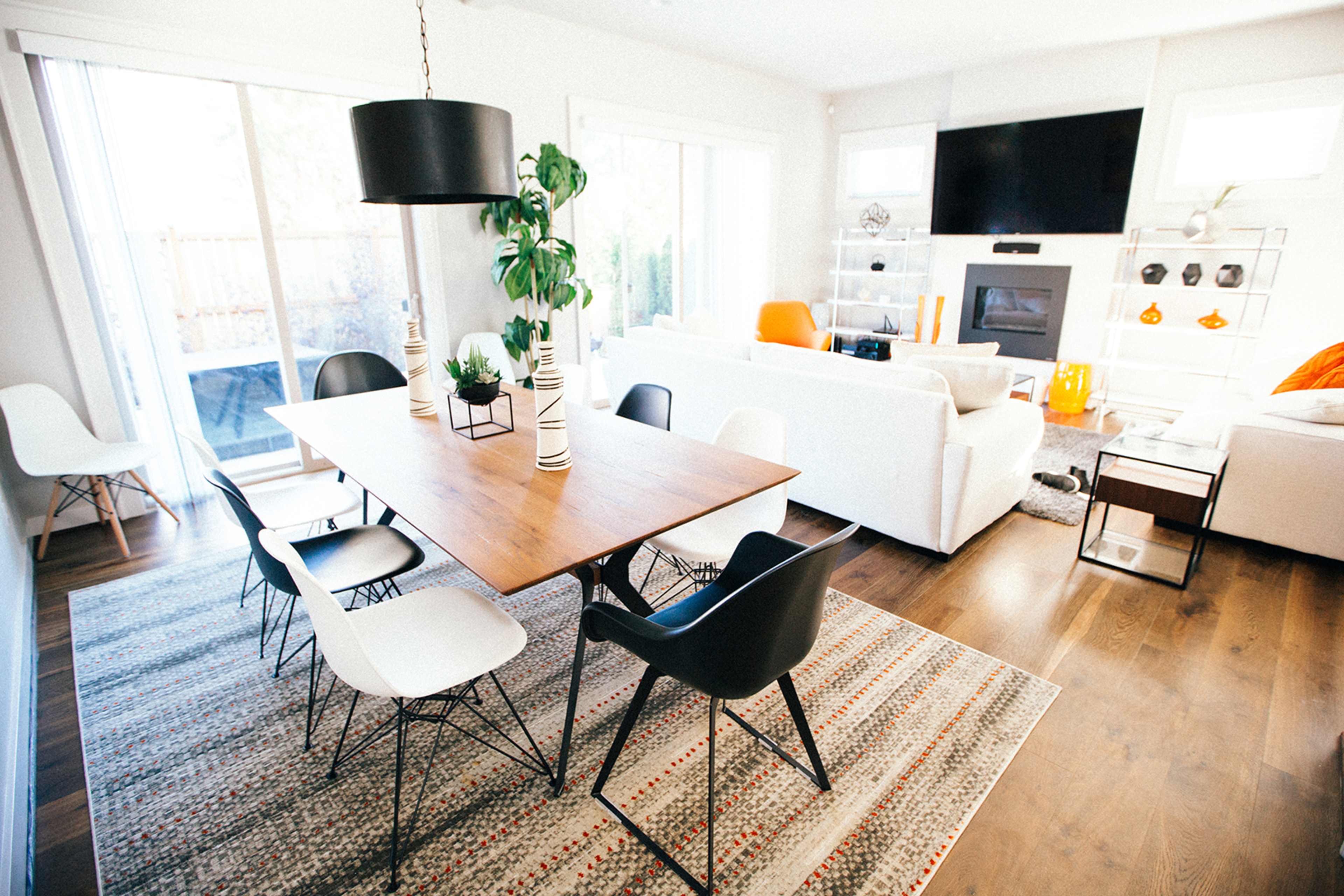 A dining area features a wooden table surrounded by black and white chairs, with large windows letting in natural light.