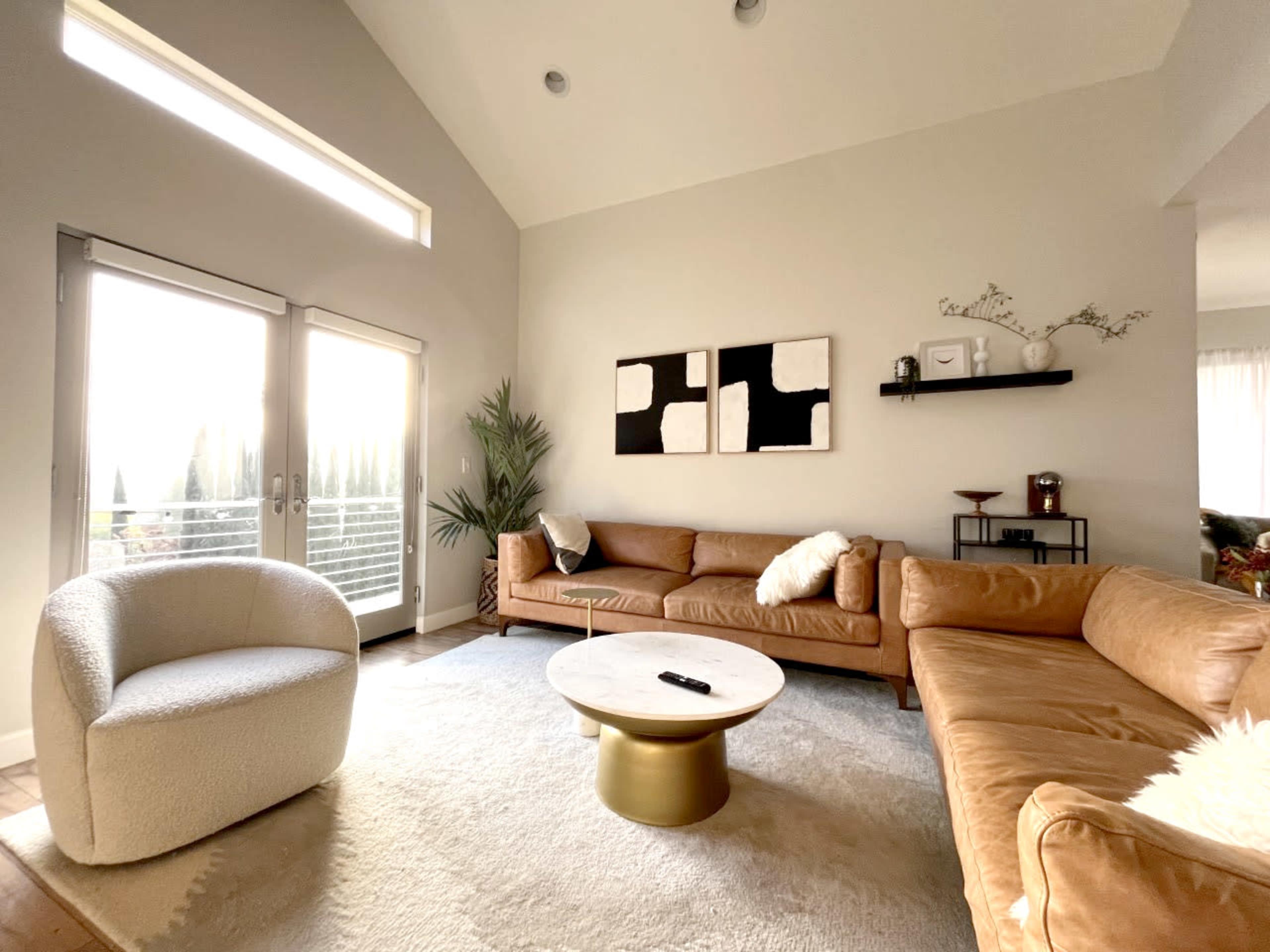 The living room features a high ceiling, a large sectional sofa, a round coffee table, and large windows that let in natural light.