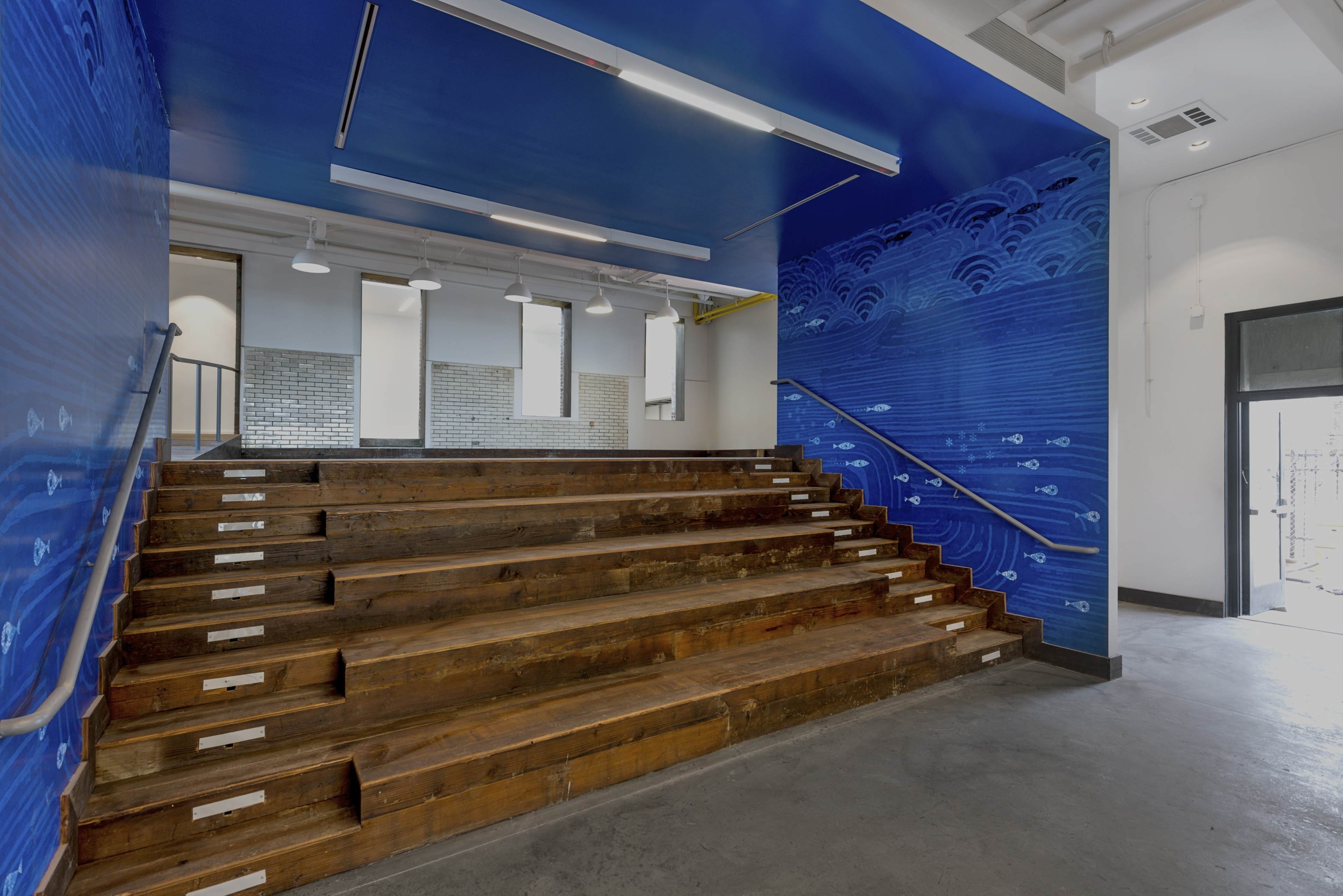 A modern indoor space with wooden steps leading up to a blue wall adorned with wave patterns.