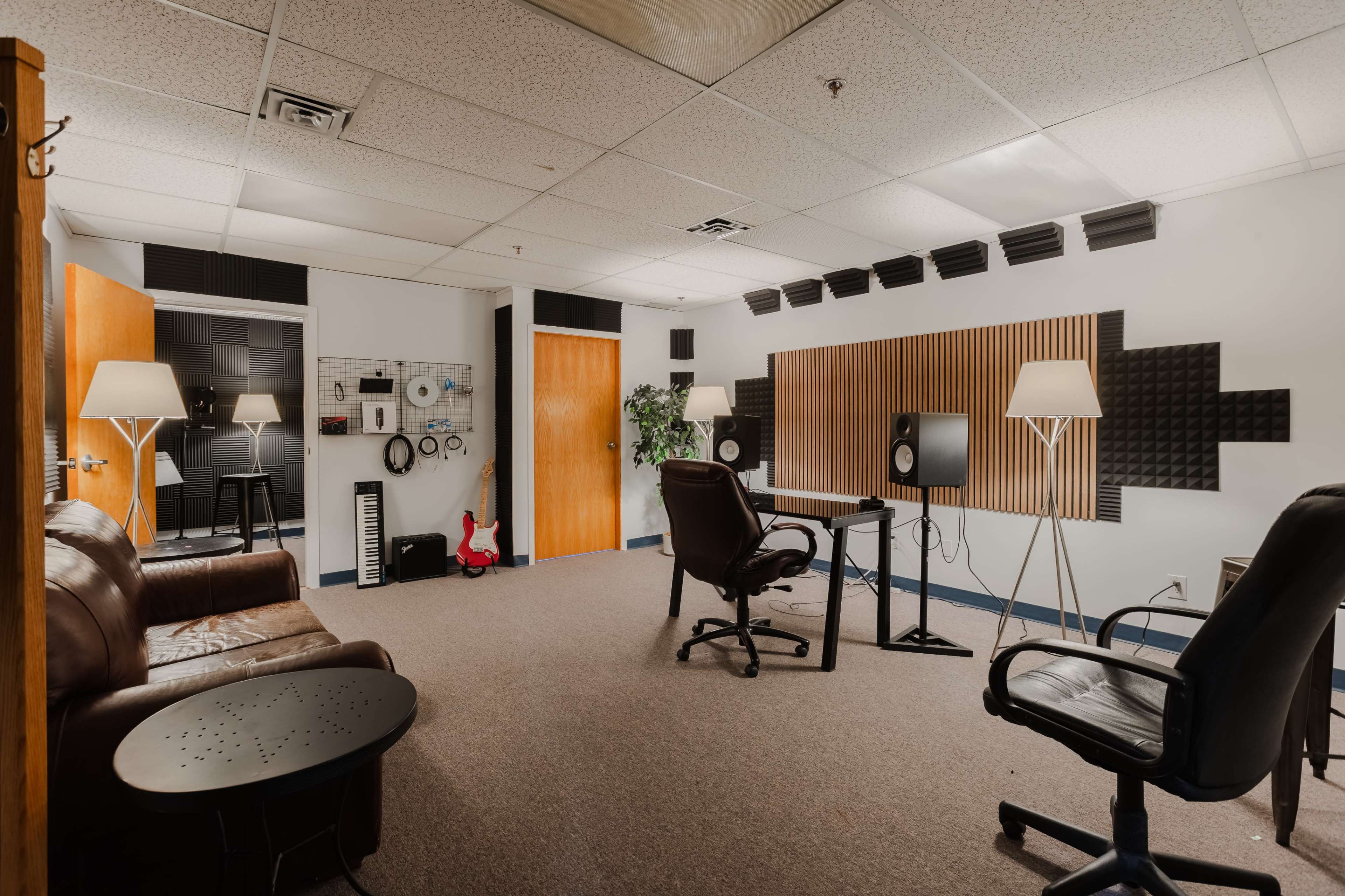 The image shows a sound studio with a comfortable seating area, a desk with audio equipment, and soundproofing panels on the walls.