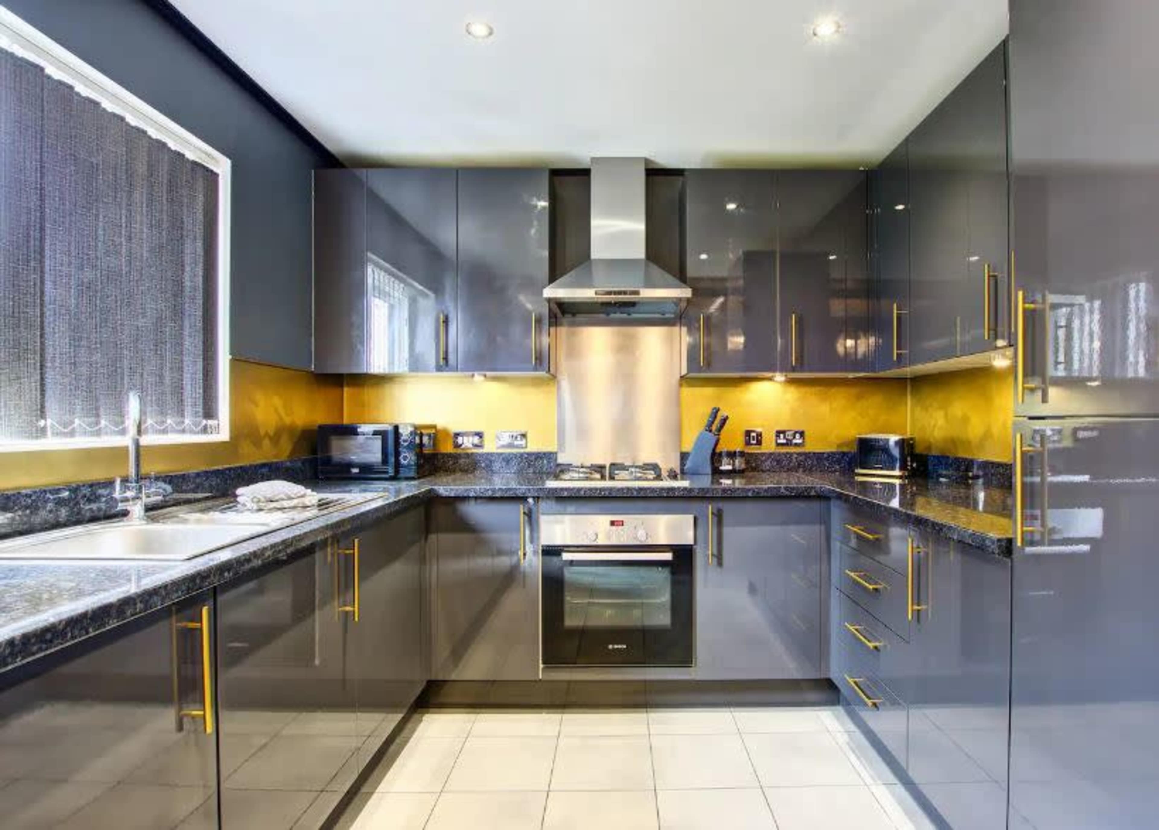 The image shows a modern kitchen featuring sleek gray cabinets, a stainless steel oven, and a yellow accent wall.