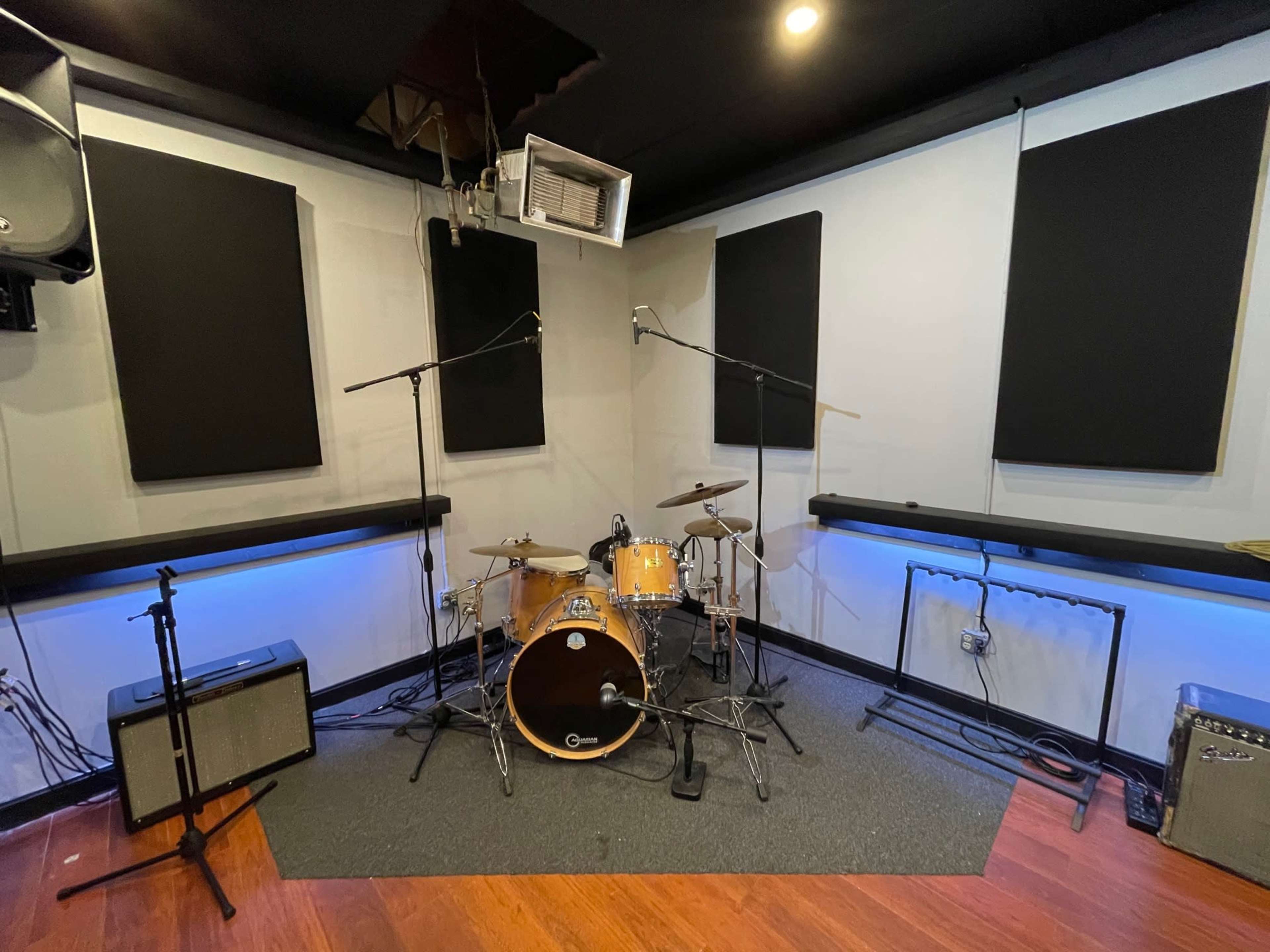 A music recording studio with a drum set, two microphones, amplifiers, and sound-absorbent wall panels.