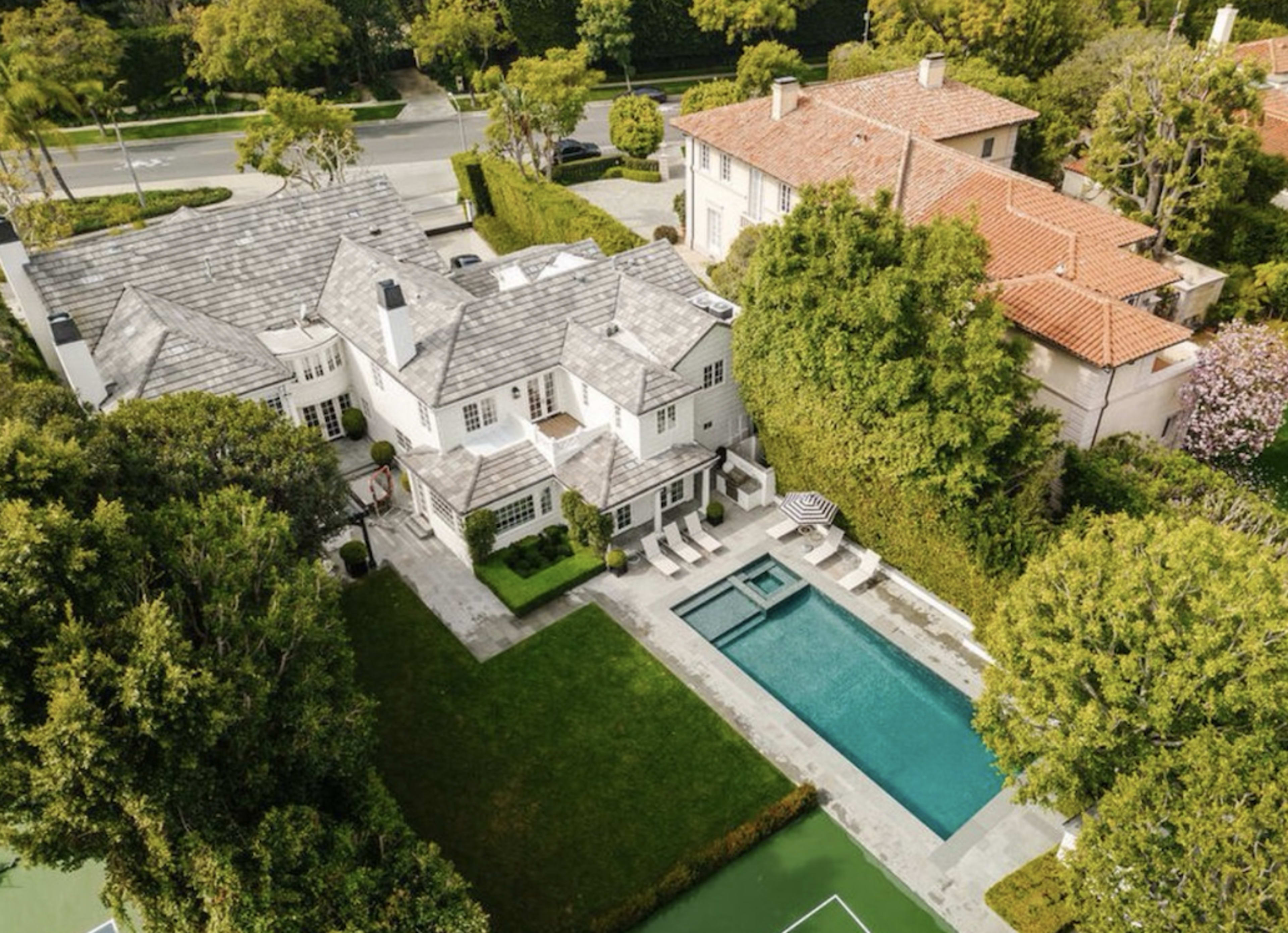The image shows a large, two-story house surrounded by greenery, with a swimming pool and outdoor seating area, located in a suburban neighborhood.