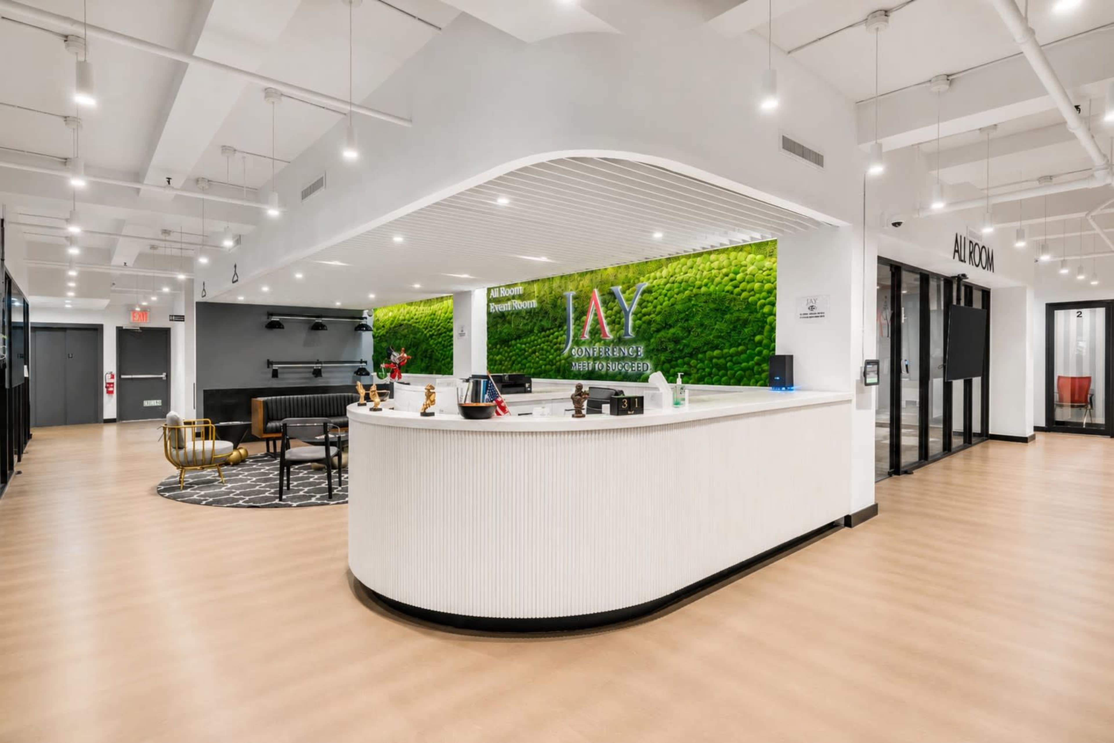 The image shows a modern office reception area with a curved white desk, a green moss wall feature, and various seating arrangements.